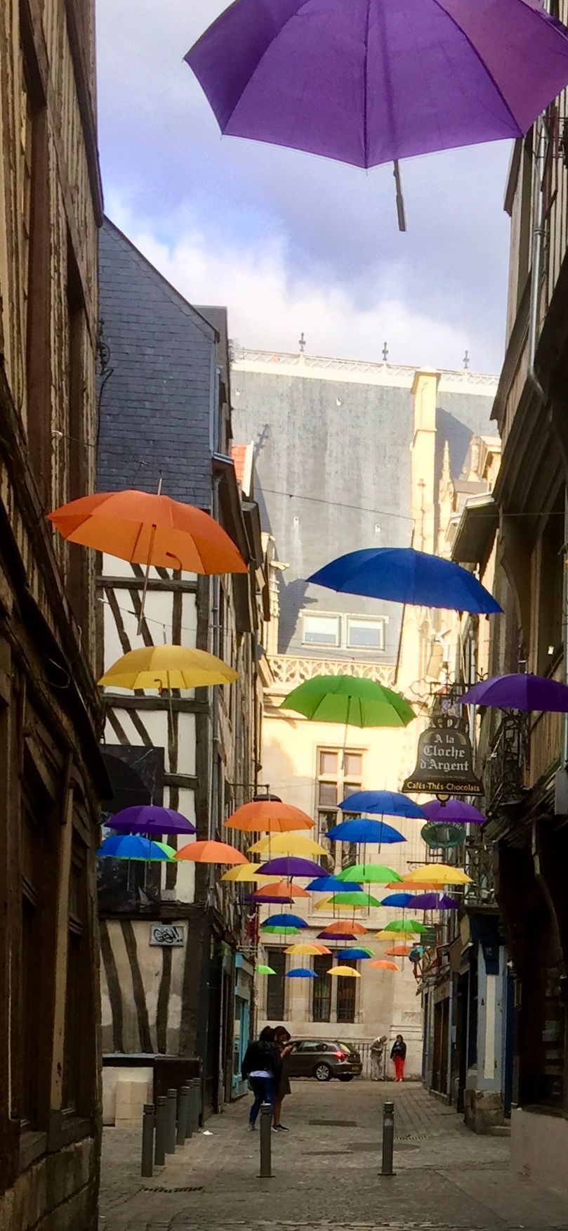 A row of colorful umbrellas are hanging from the ceiling of an alleyway.