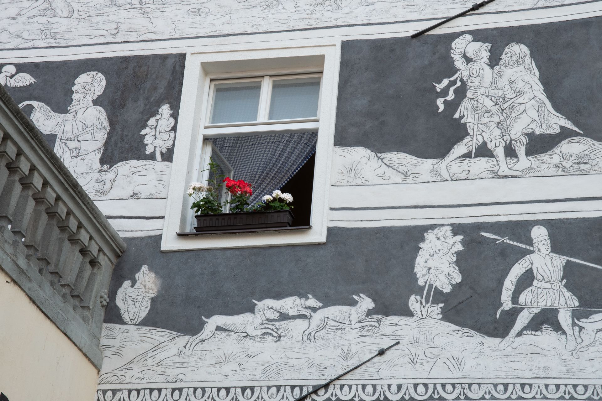 A window with flowers in it and a painting on the side of a building