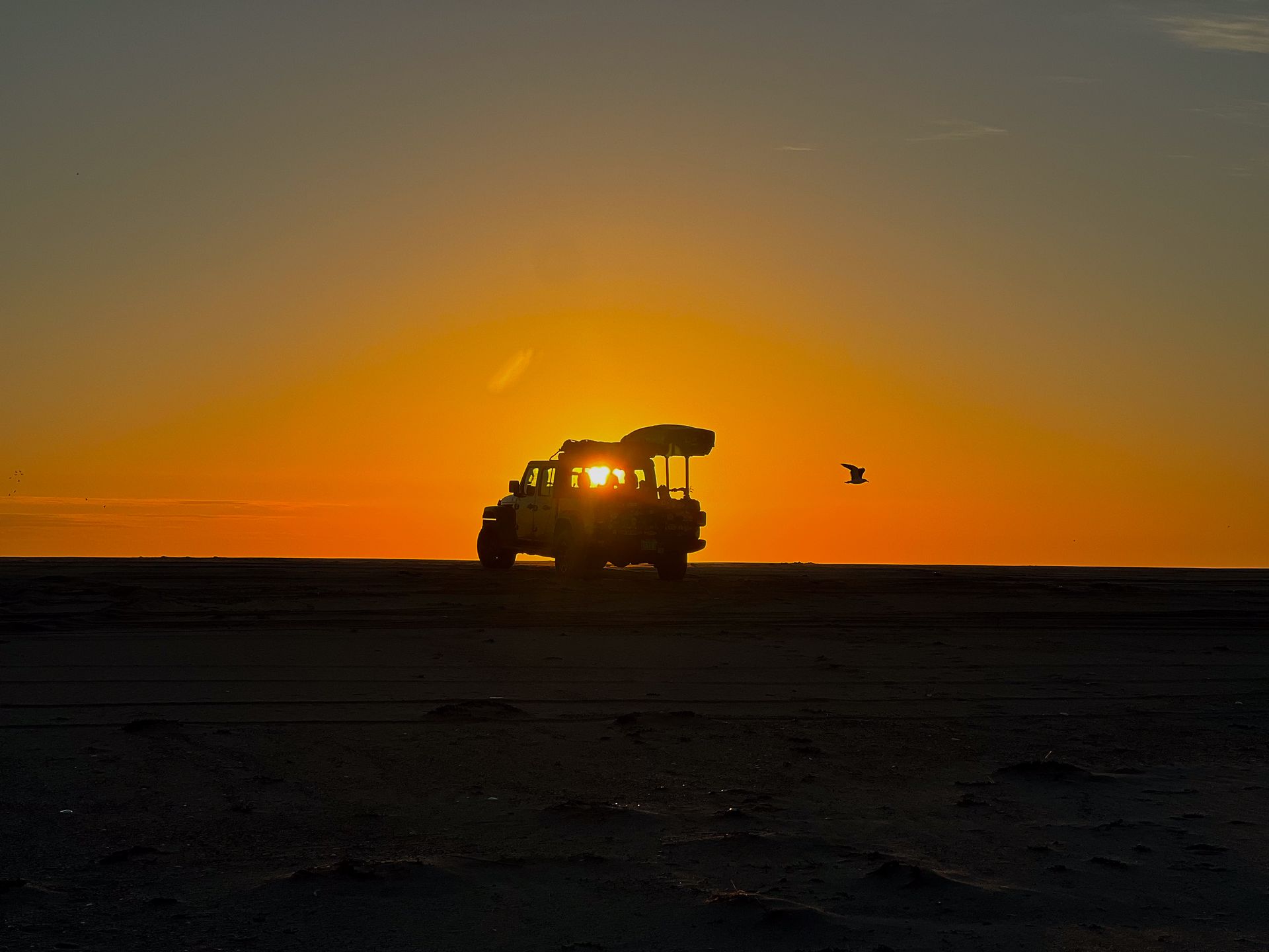 a jeep is driving through the desert at sunset .