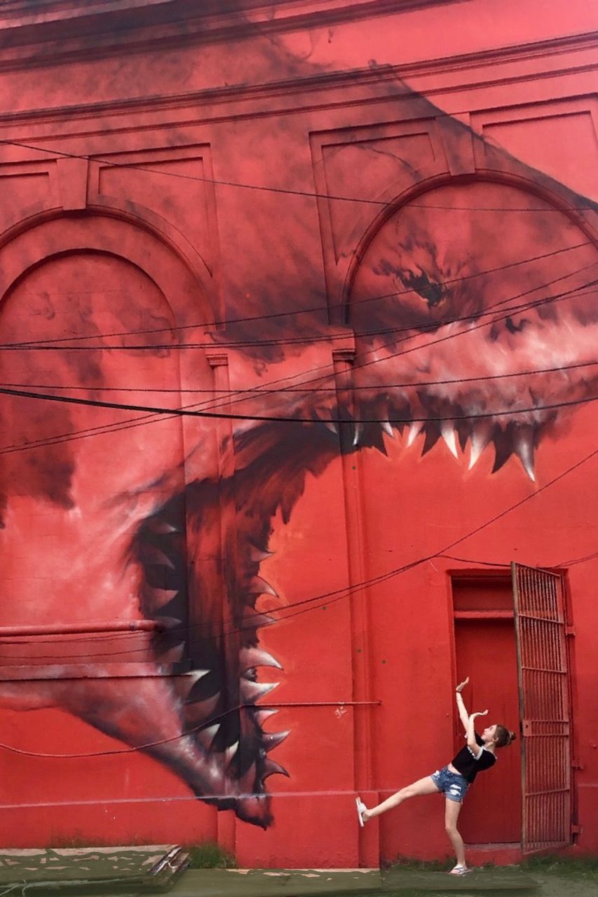 A woman is standing in front of a mural of a shark 's mouth on a red wall.