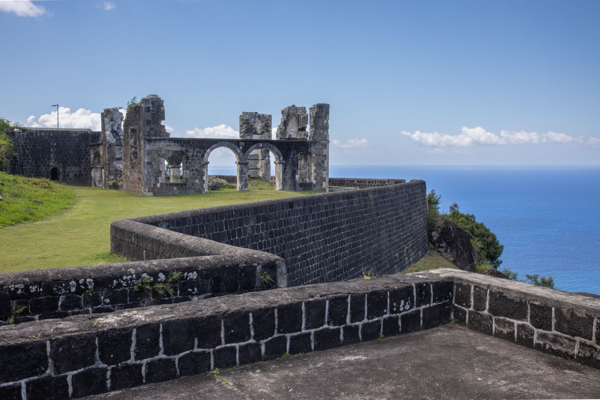 A stone wall surrounds a castle on a hill overlooking the ocean.