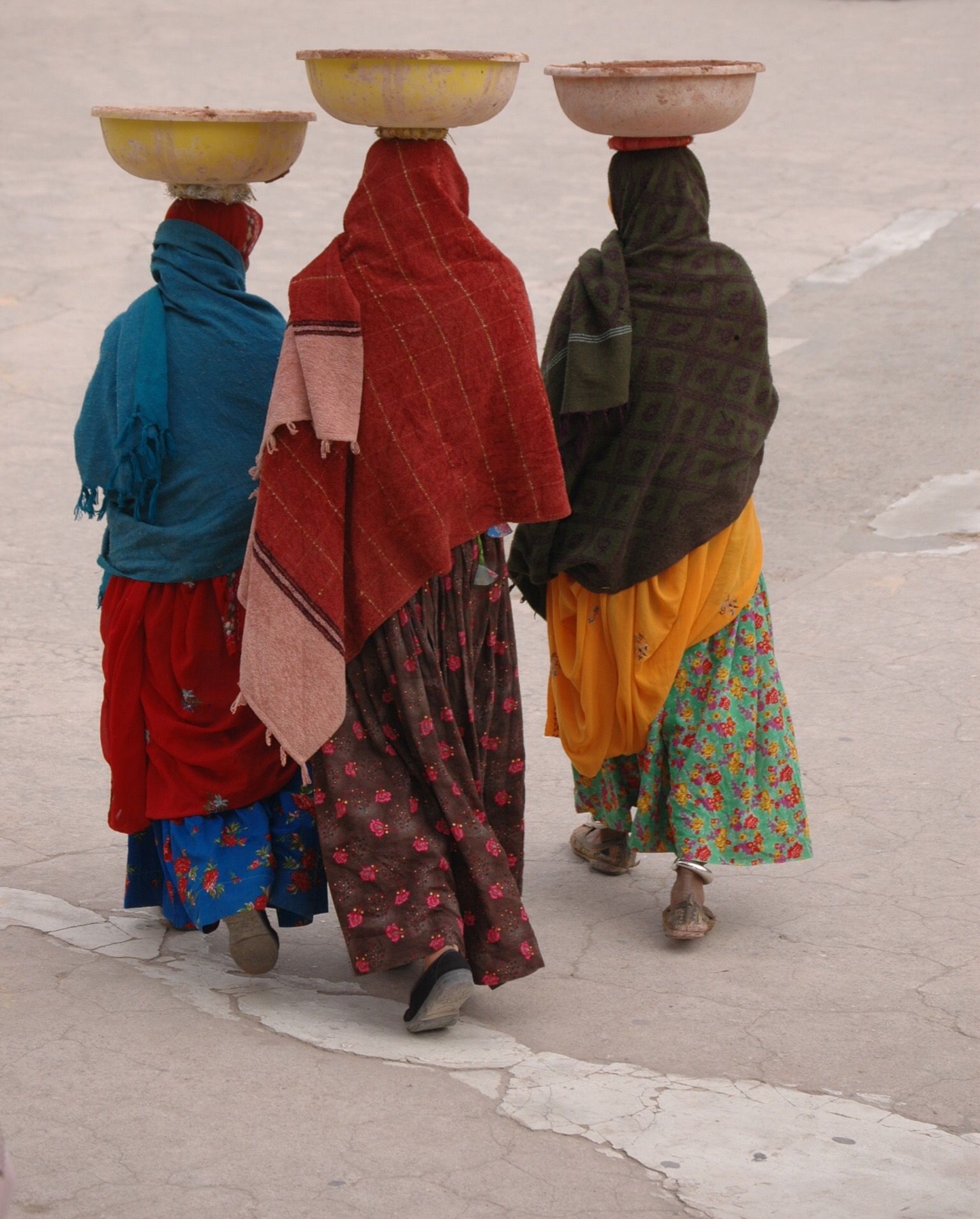 Three women are walking with bowls on their heads