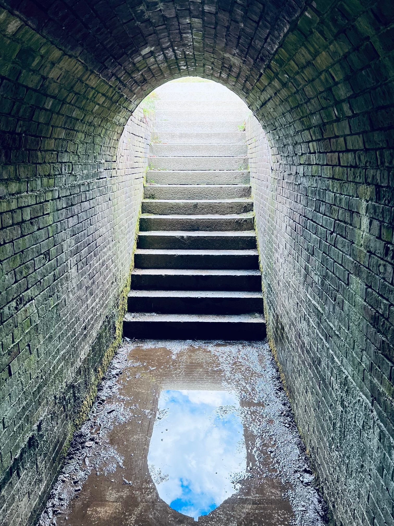 A brick tunnel with stairs leading up to the light at the end.