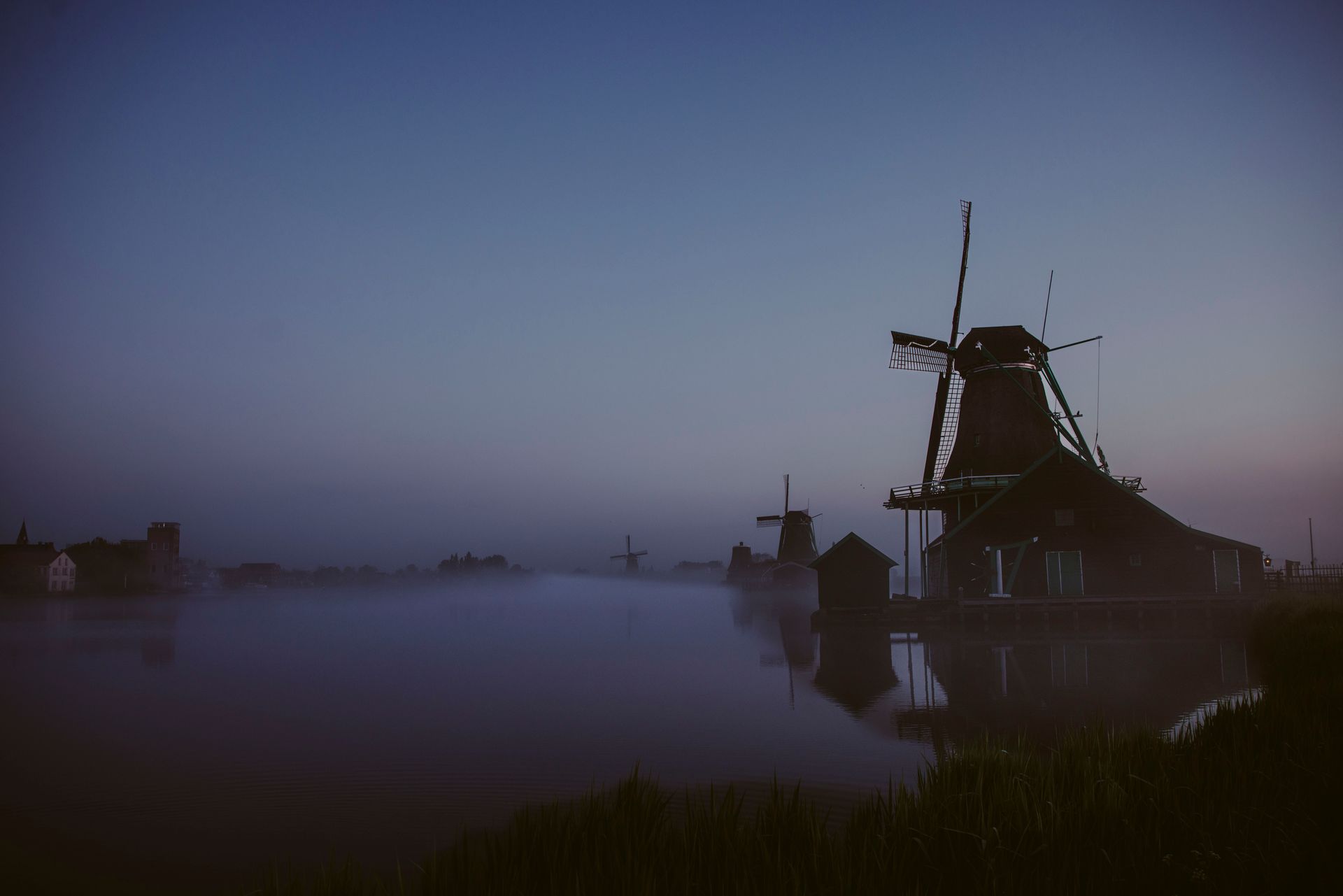 A group of windmills are silhouetted against a foggy sky.