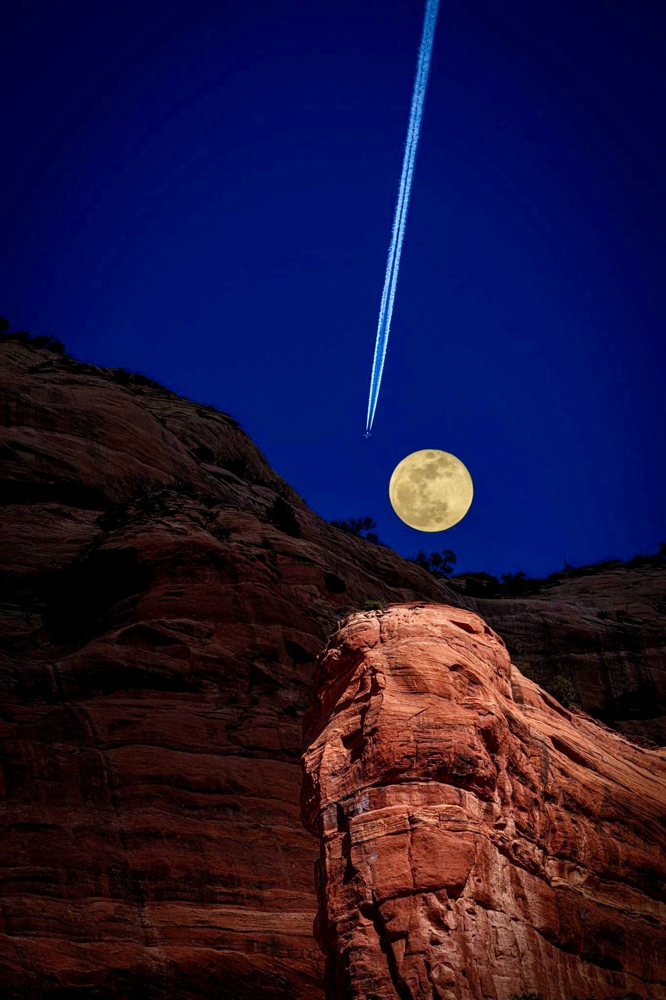 A full moon is rising over a rocky cliff at night.