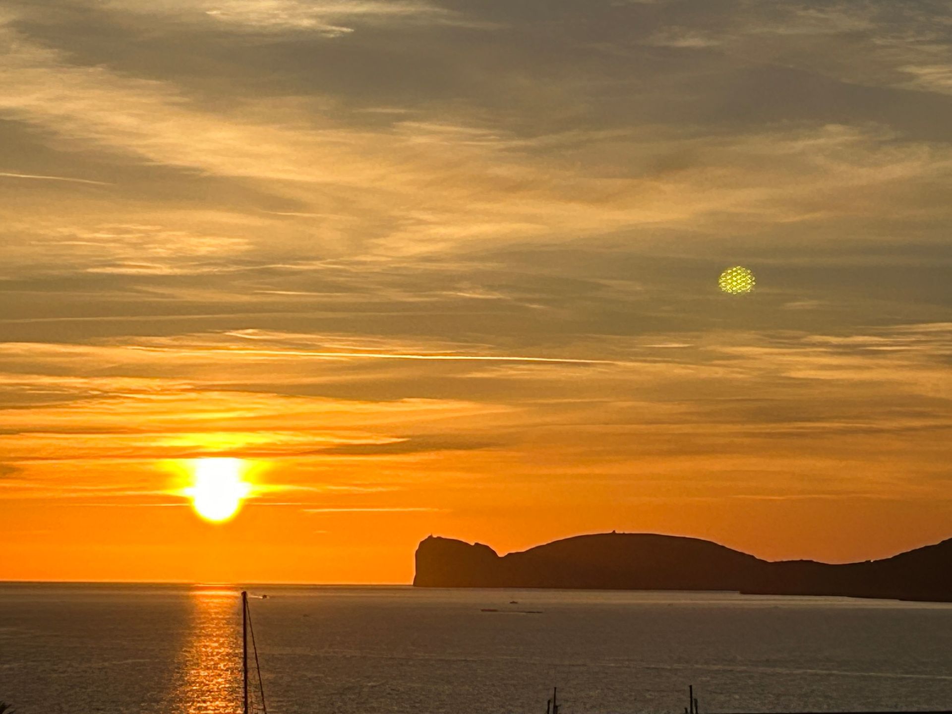 The sun is setting over the ocean with a mountain in the background.