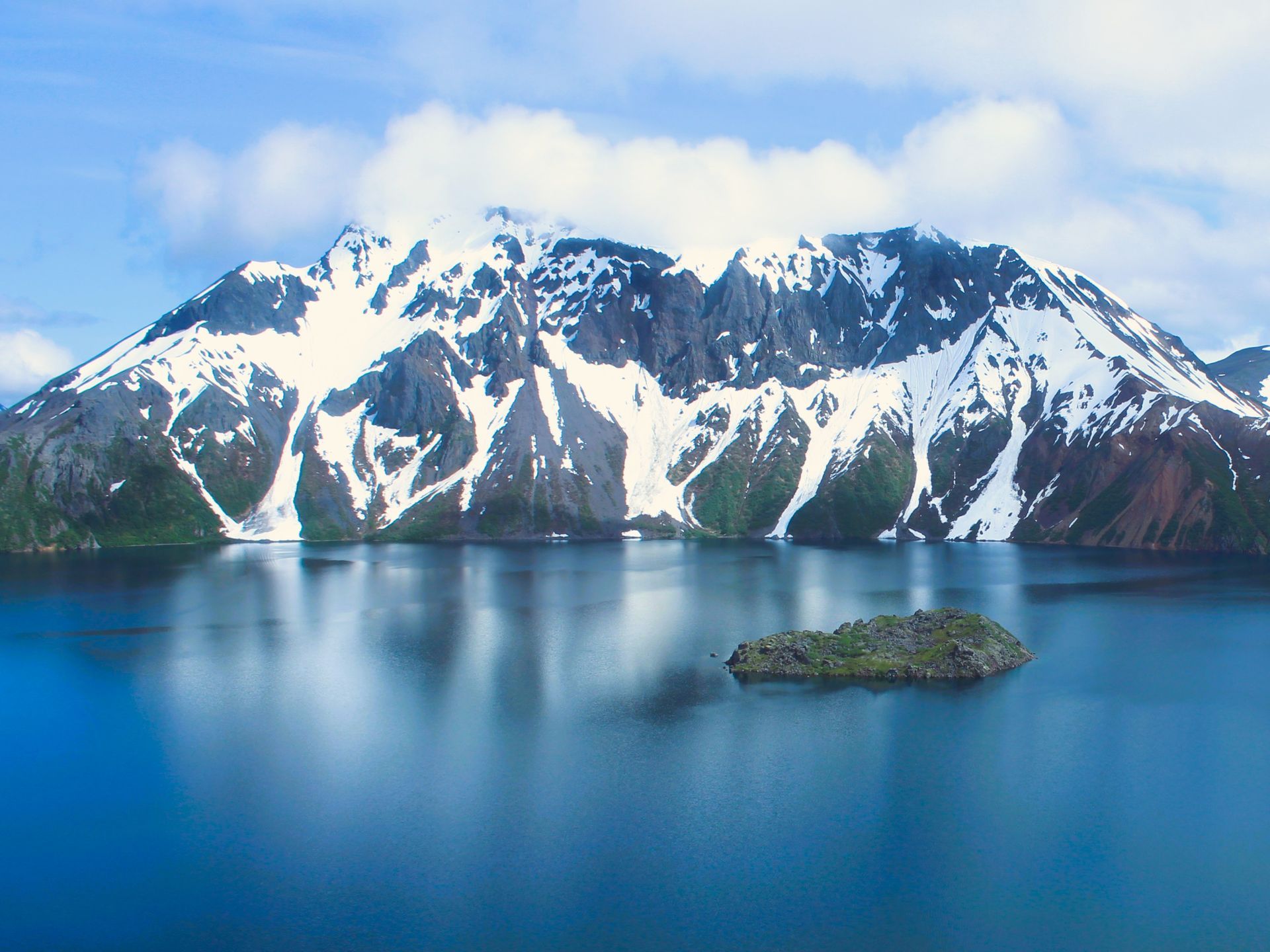 A small island in the middle of a lake with mountains in the background.
