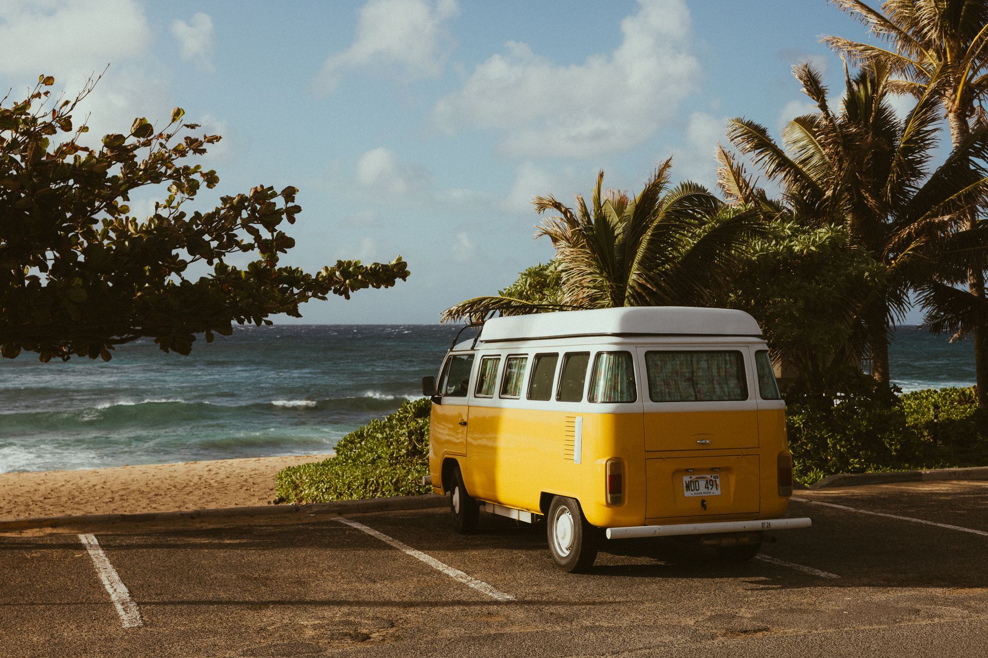 A yellow van is parked in a parking lot near the beach.
