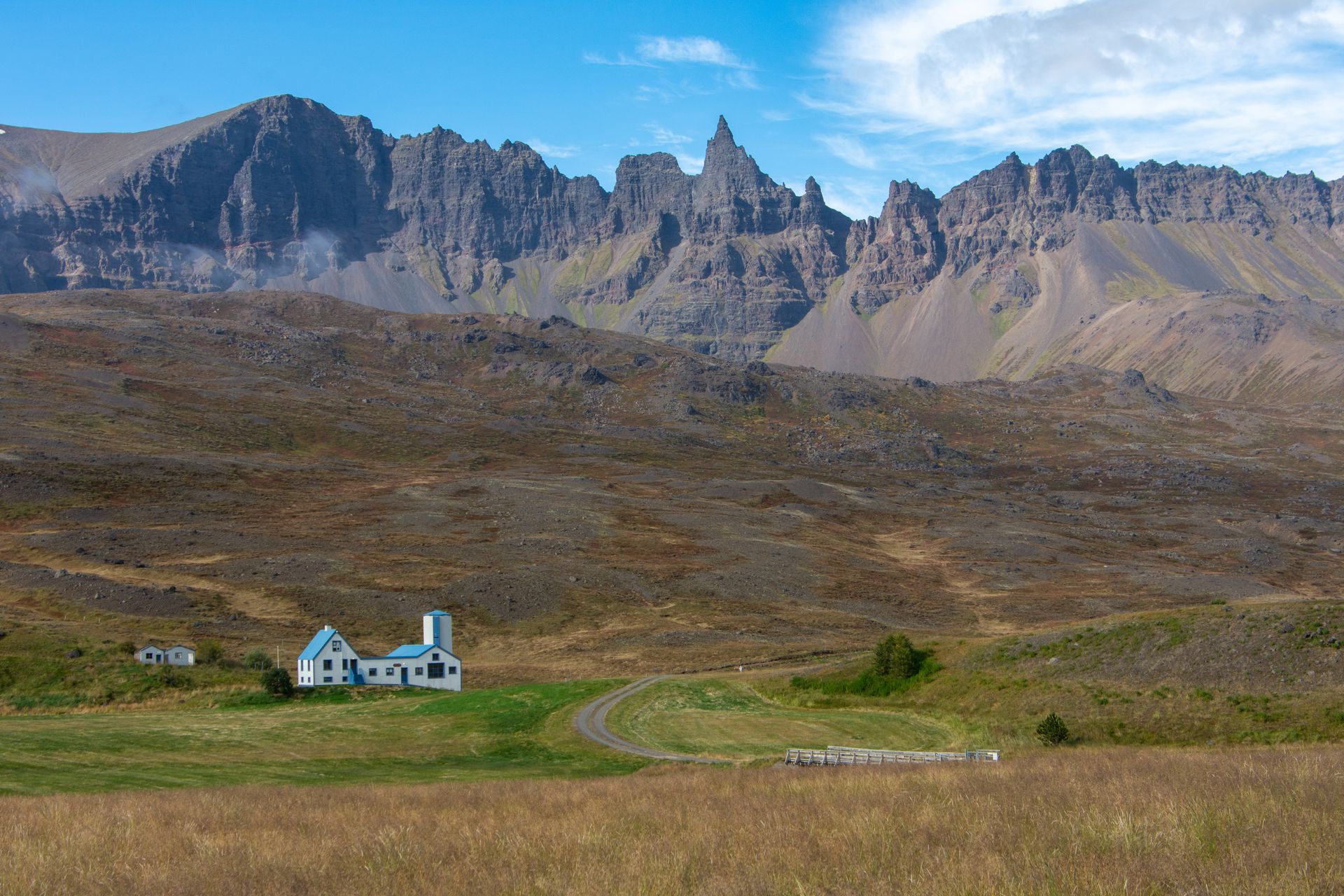 A small house in the middle of a field with mountains in the background.