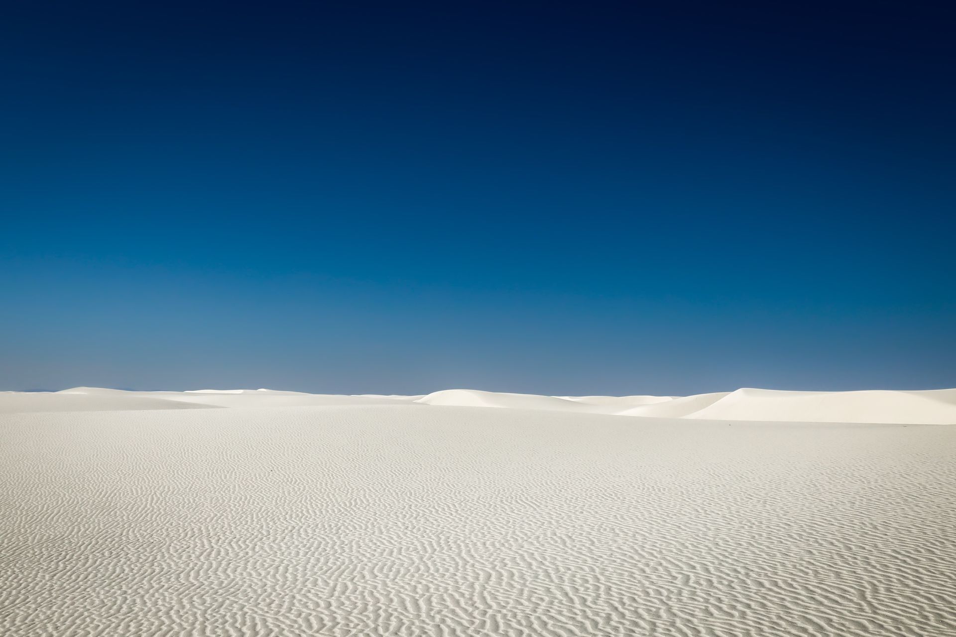 A desert landscape with white sand and a blue sky