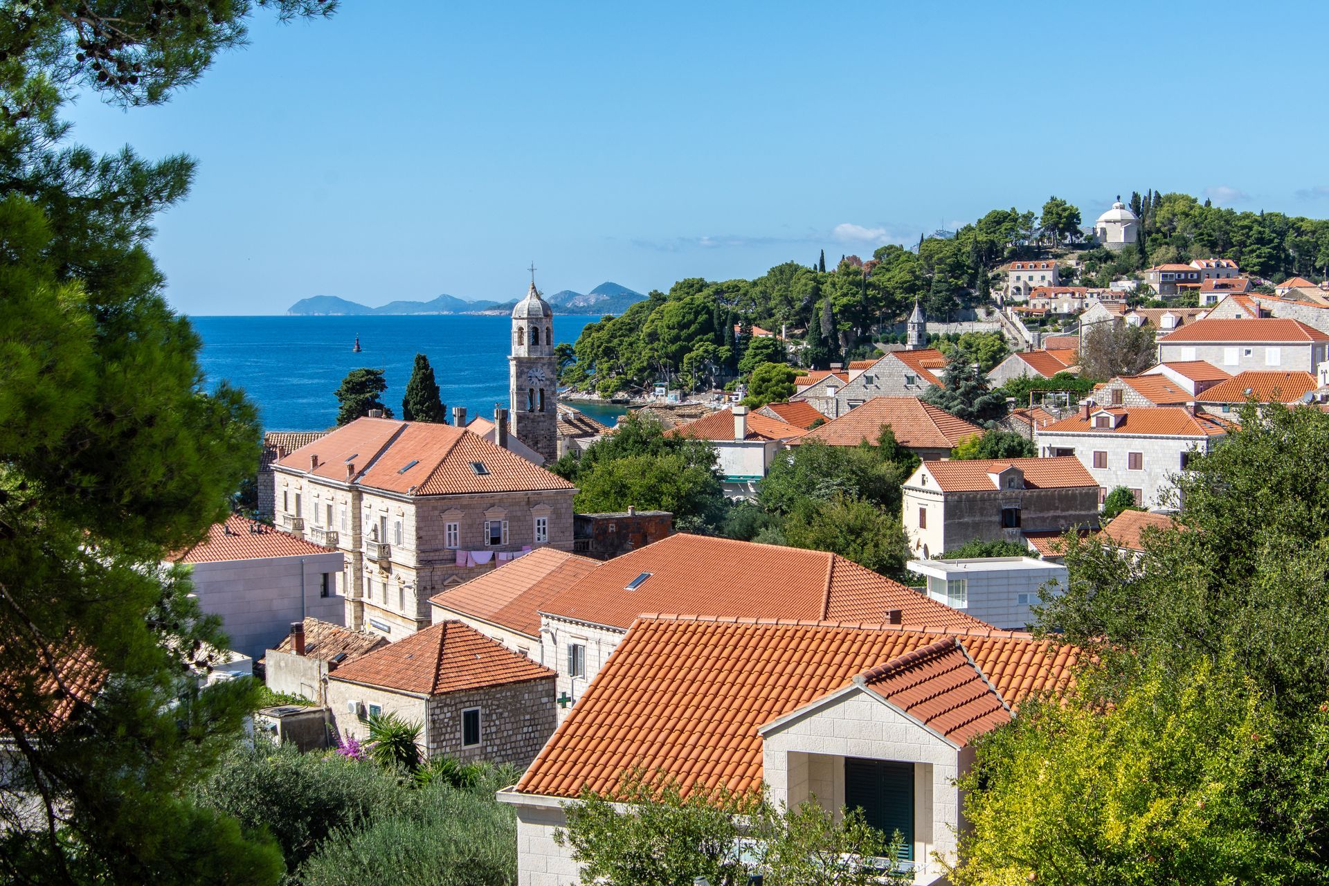 A small town with red tile roofs and a church on a hill overlooking the ocean.