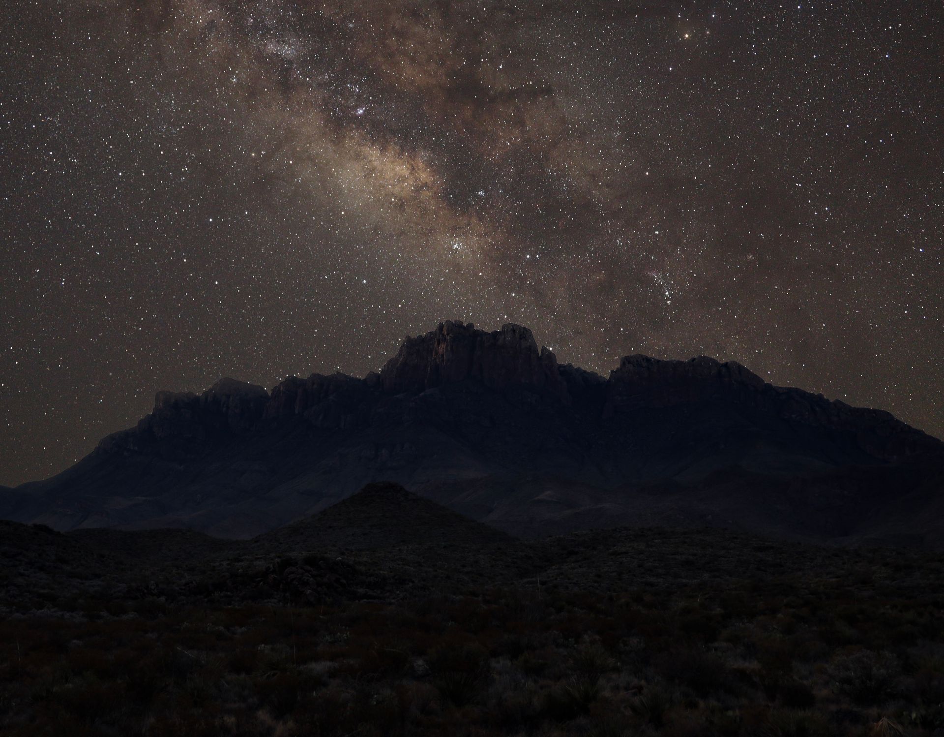 The milky way is visible over a mountain range at night.