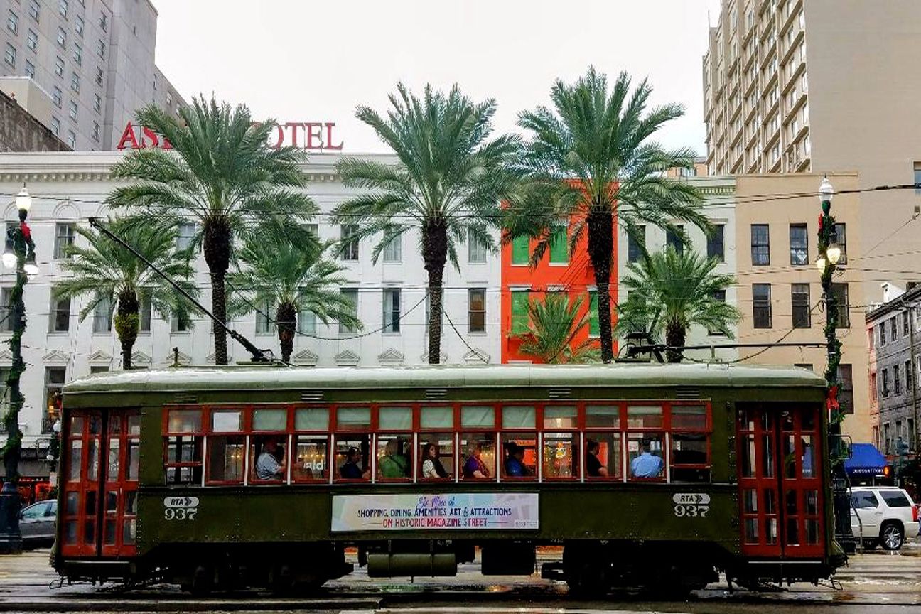 A trolley is driving down a city street in front of a hotel.