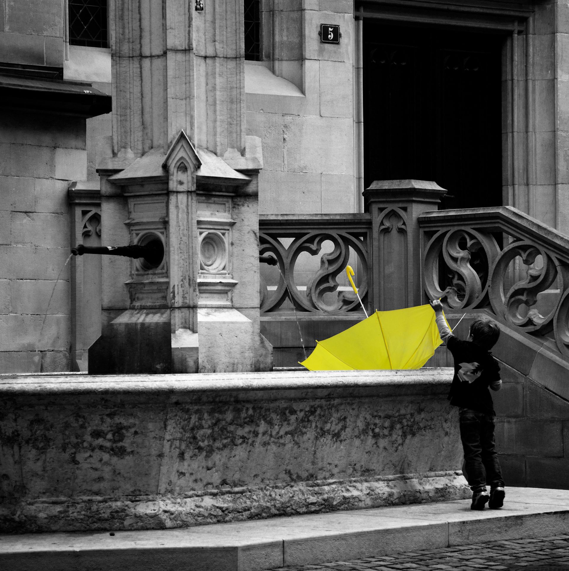 A black and white photo of a boy holding a yellow umbrella