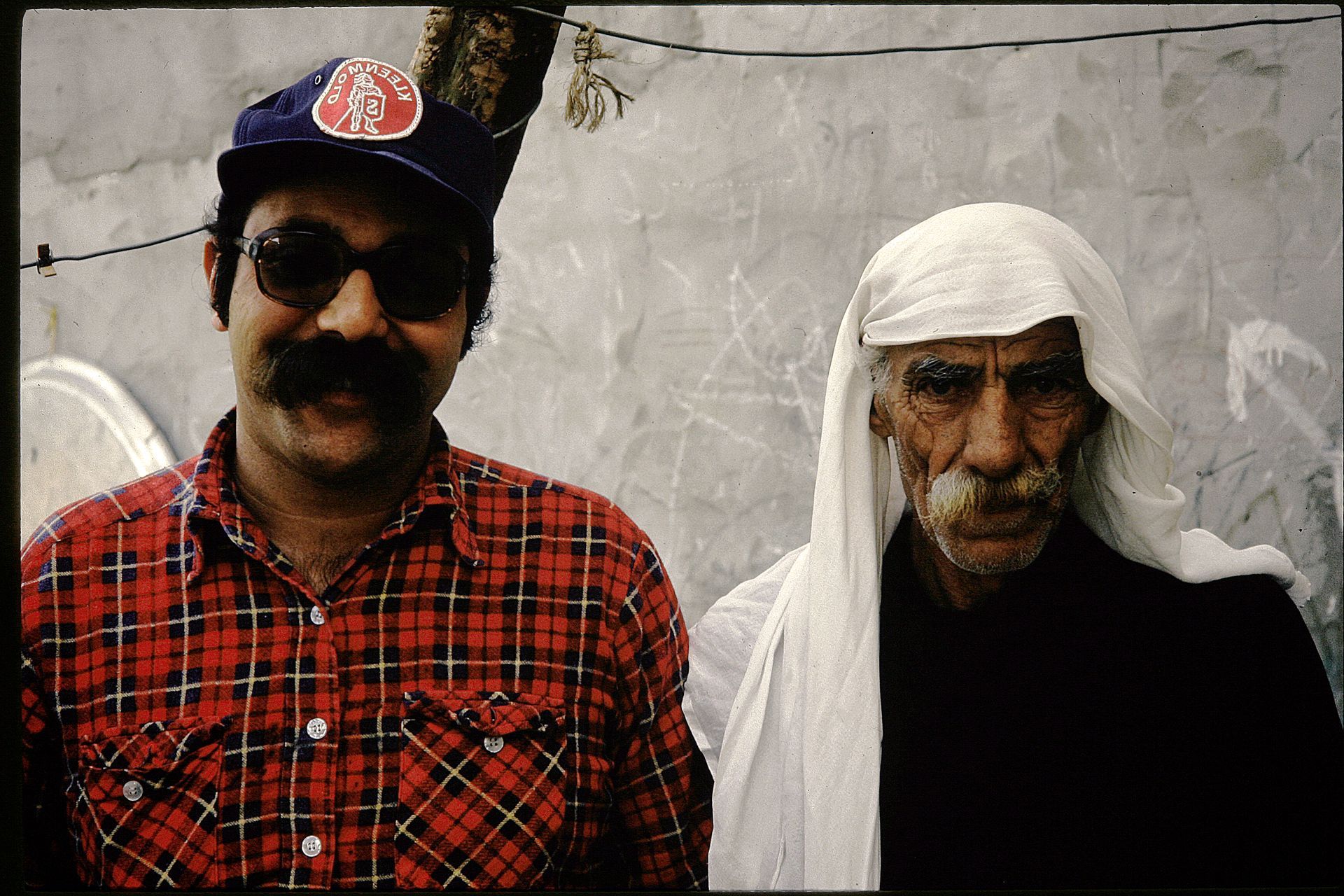 A man in a plaid shirt is standing next to an older man
