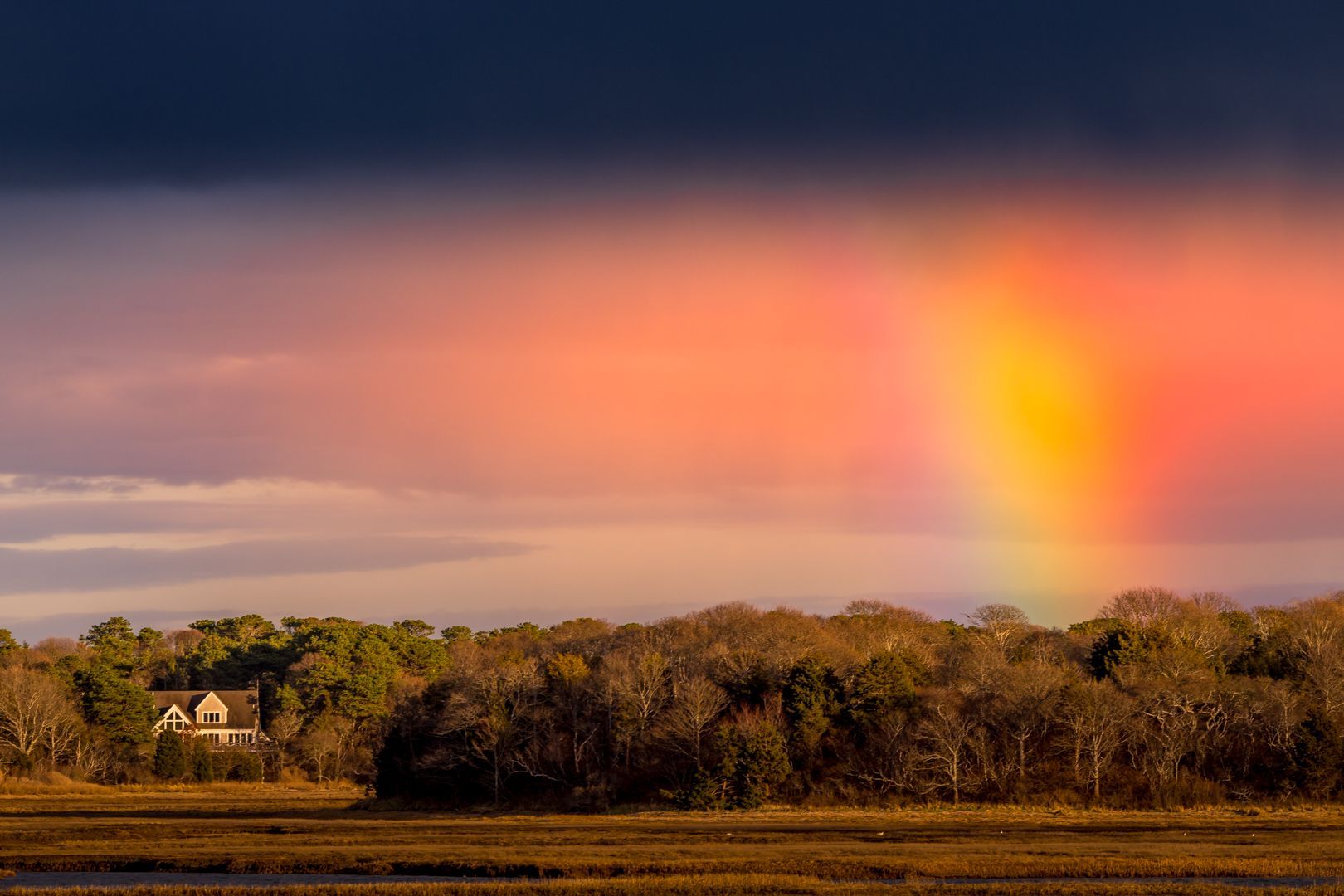 There is a rainbow in the sky over a field and trees.