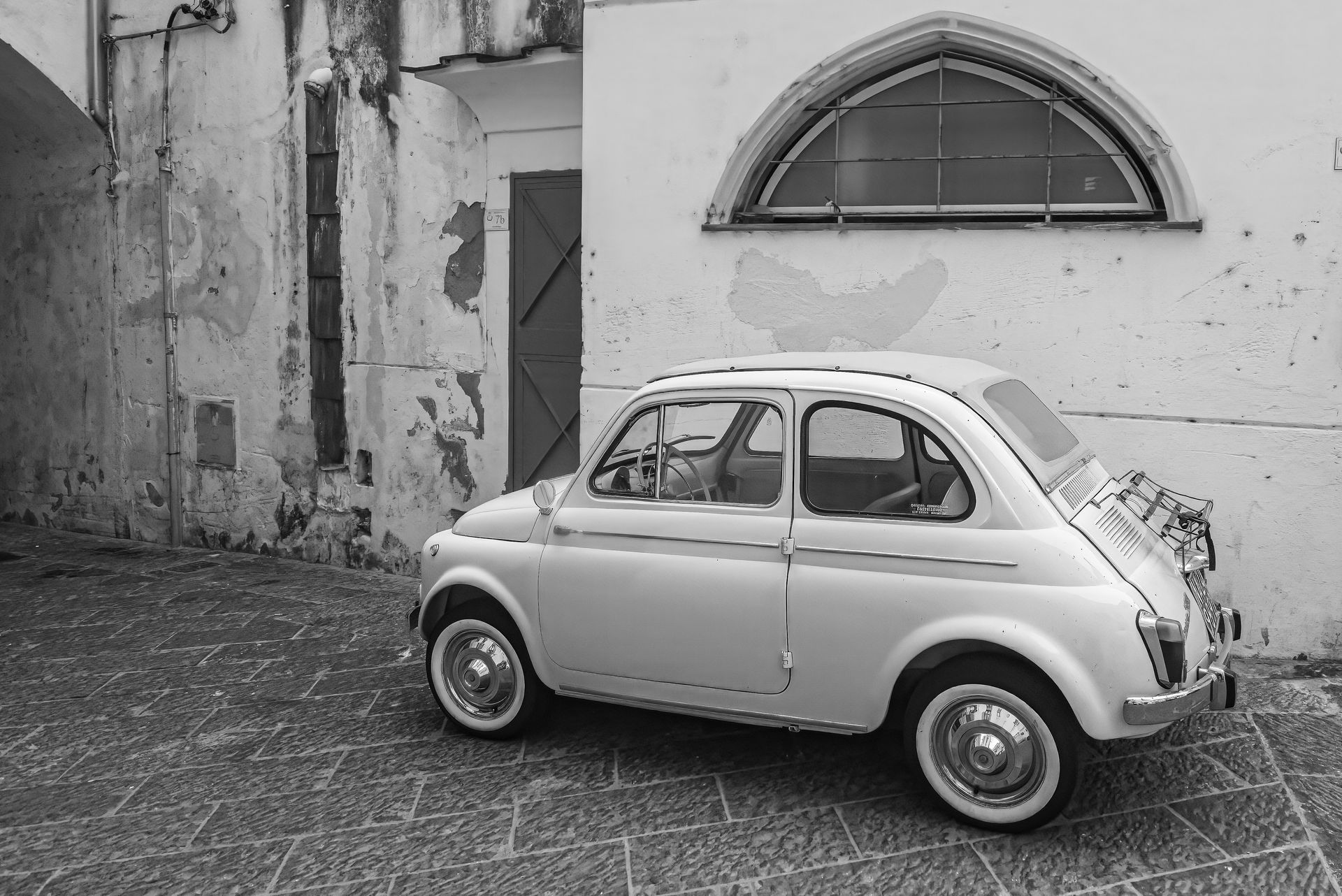 A black and white photo of a small white car parked in front of a building.