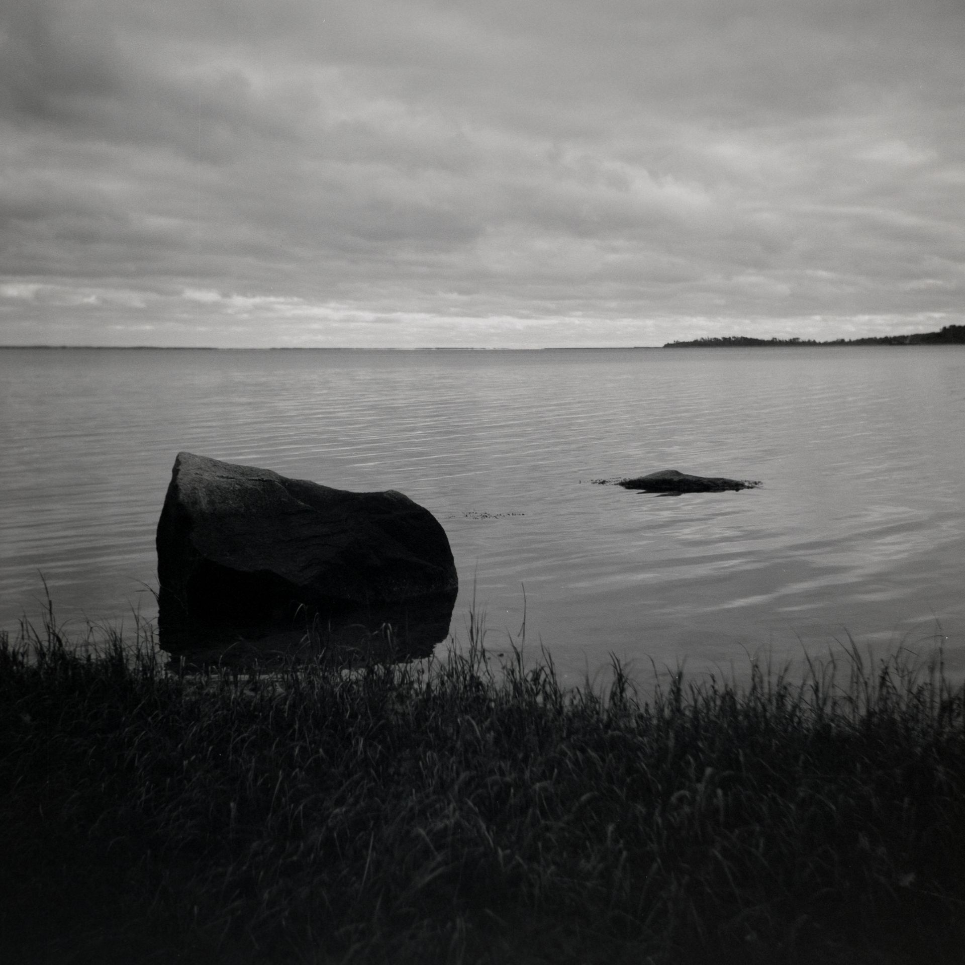 A black and white photo of a large rock in the middle of a lake.