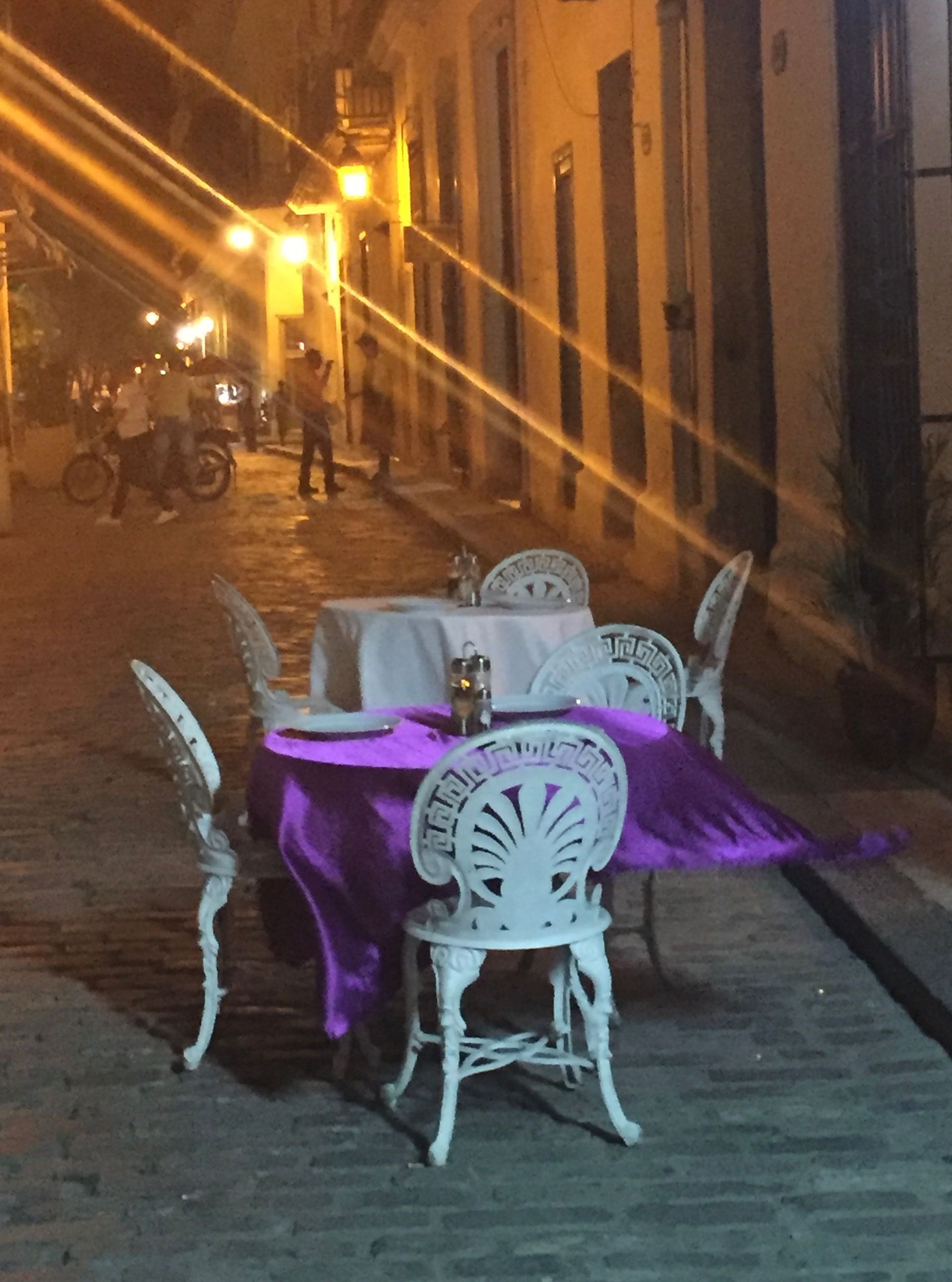 A table with a purple table cloth and white chairs