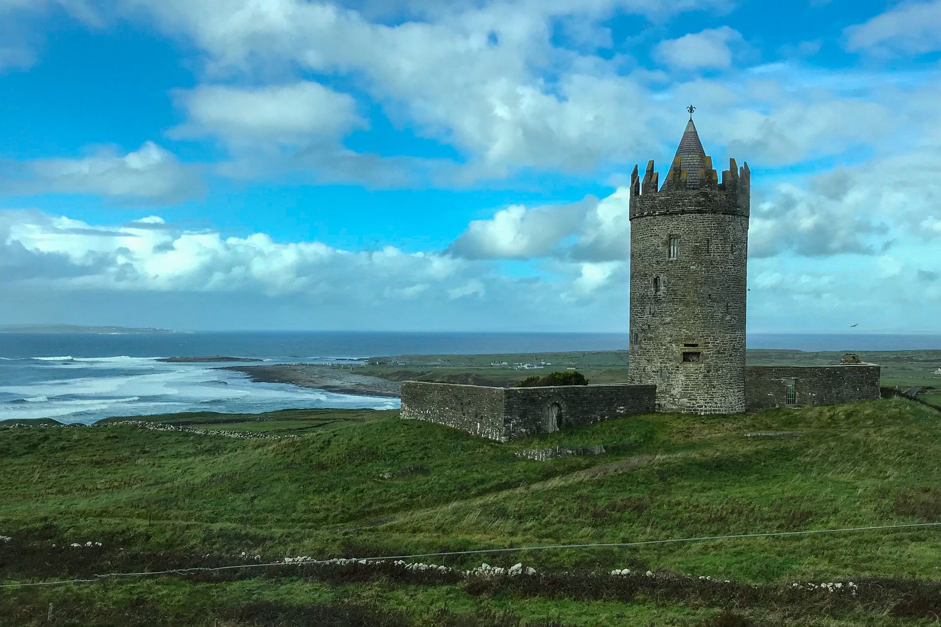 A castle tower sitting on top of a grassy hill overlooking the ocean.