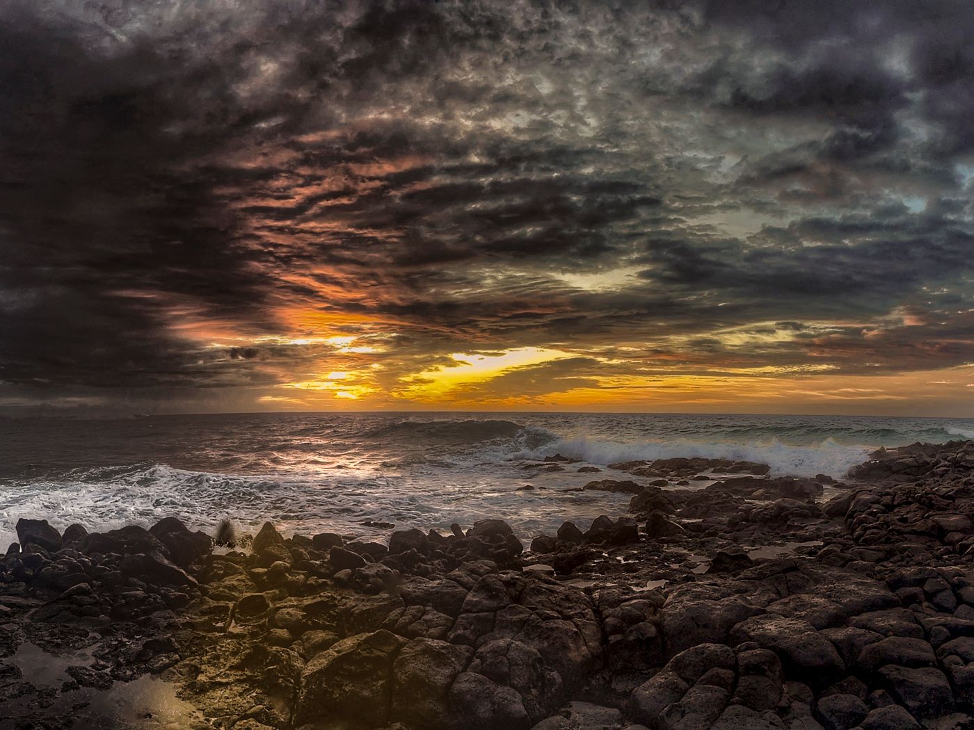 A sunset over the ocean with a rocky shoreline in the foreground.