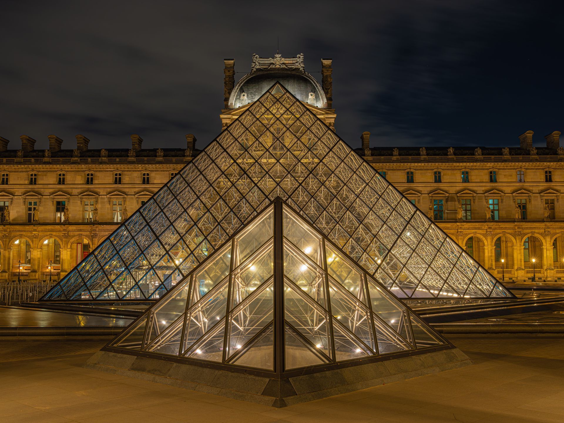 A large glass pyramid is lit up at night in front of a building.