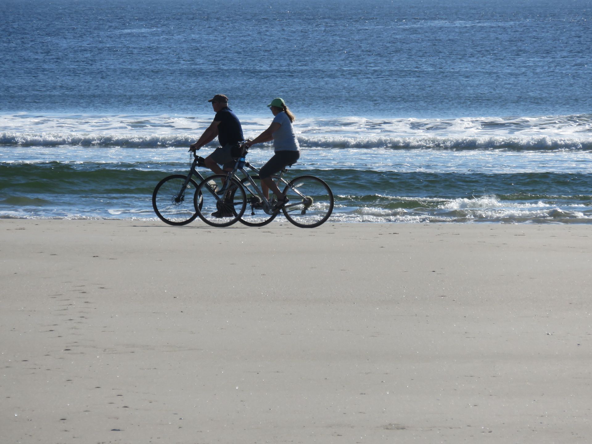 A man and a woman are riding bicycles on the beach