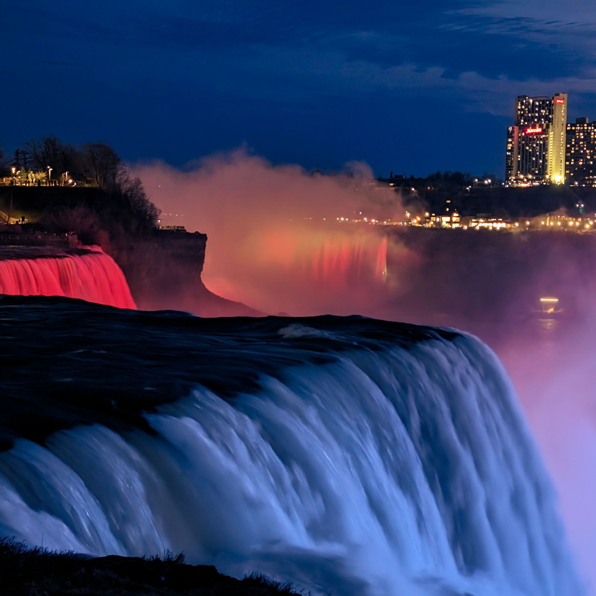 A waterfall is lit up at night with a city in the background