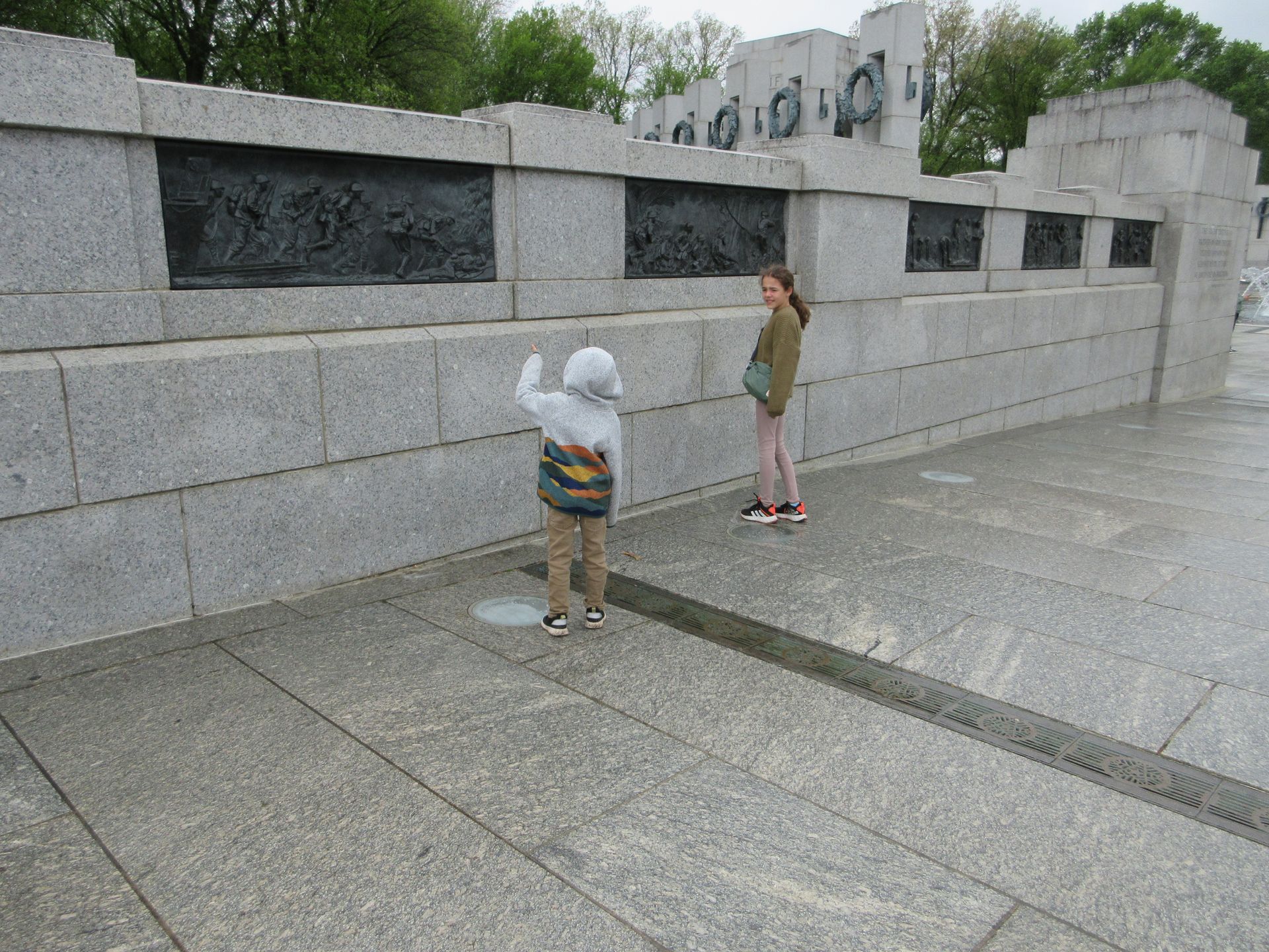 A boy and a girl are standing in front of a stone wall.