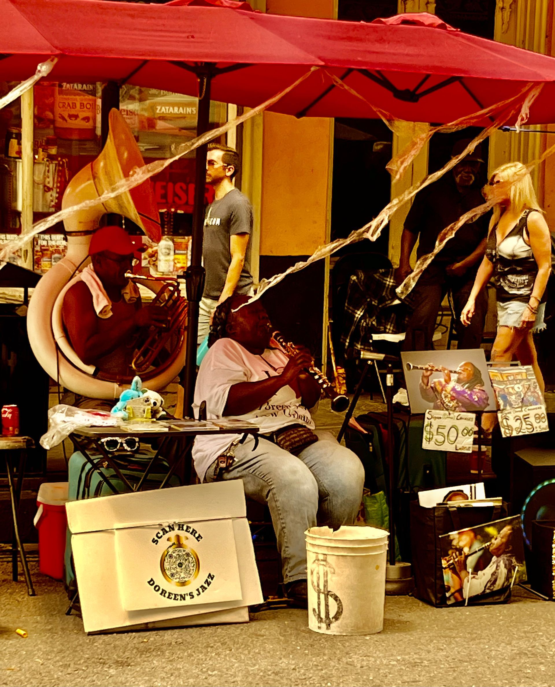 A woman sits under an umbrella playing a trumpet