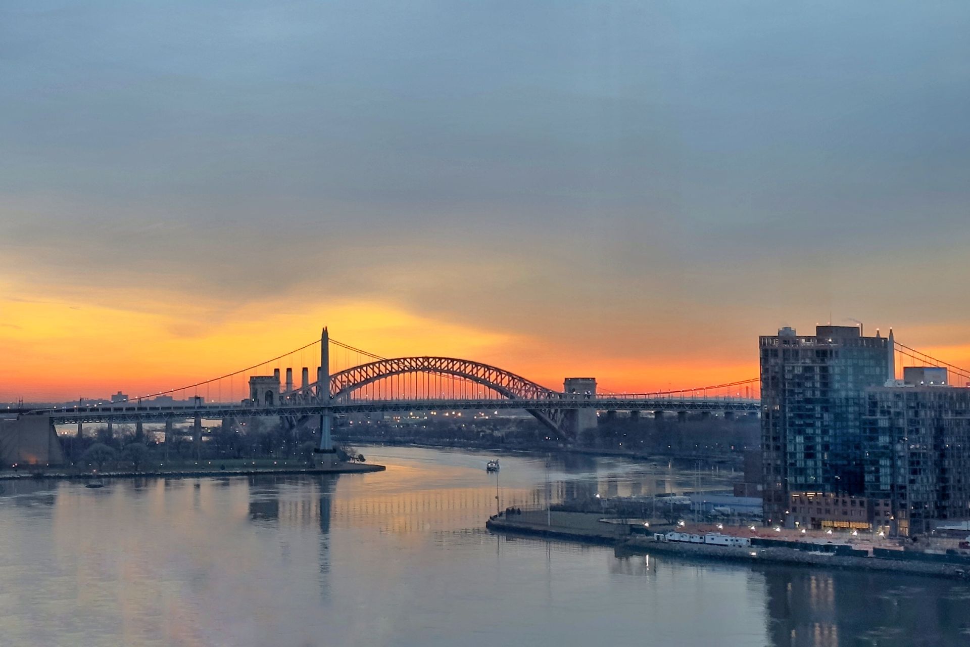 A bridge over a body of water with a city in the background at sunset.