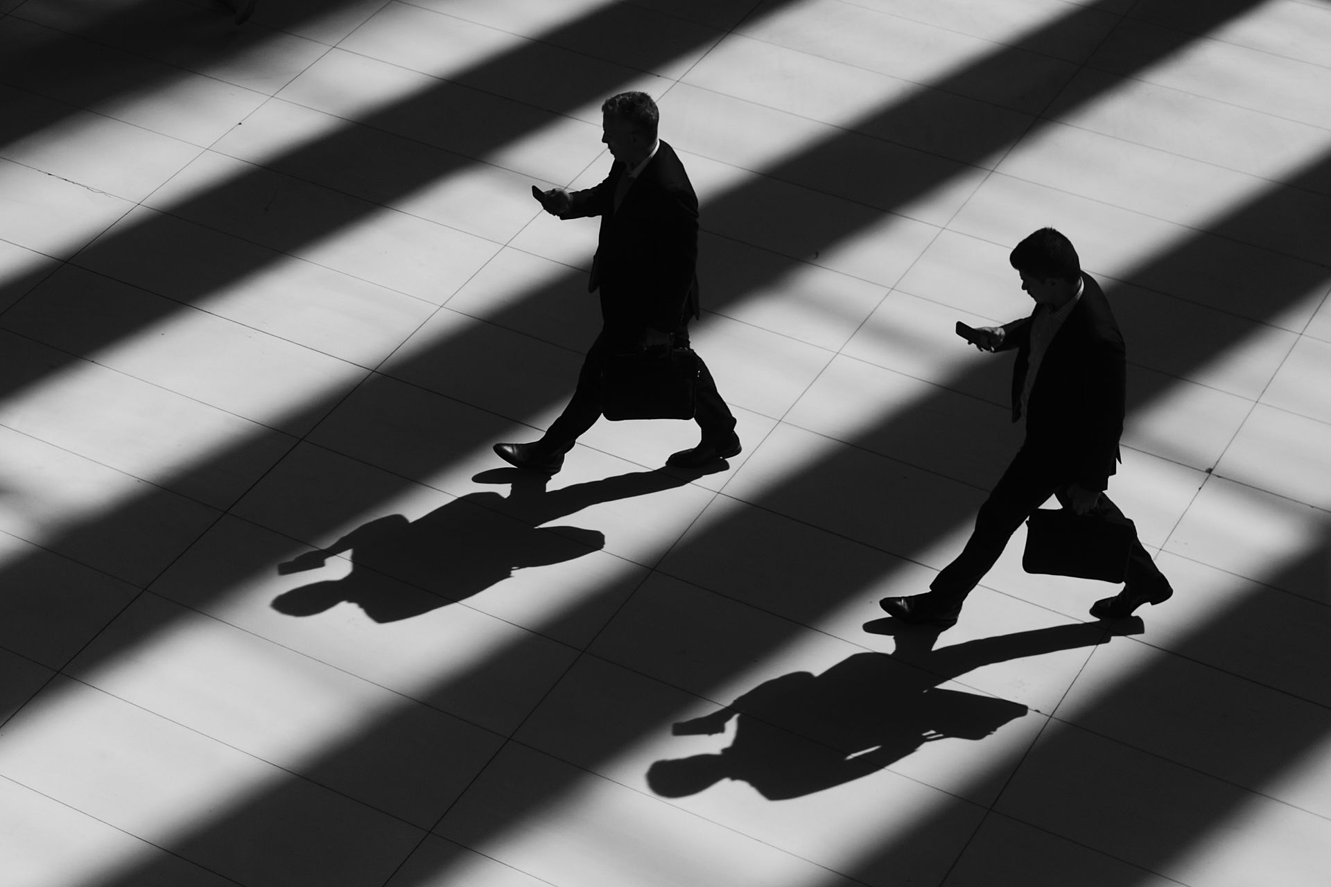 A black and white photo of two people walking in the shadows