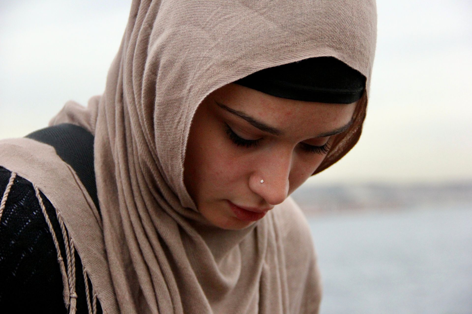 A woman wearing a hijab and a nose ring looks down