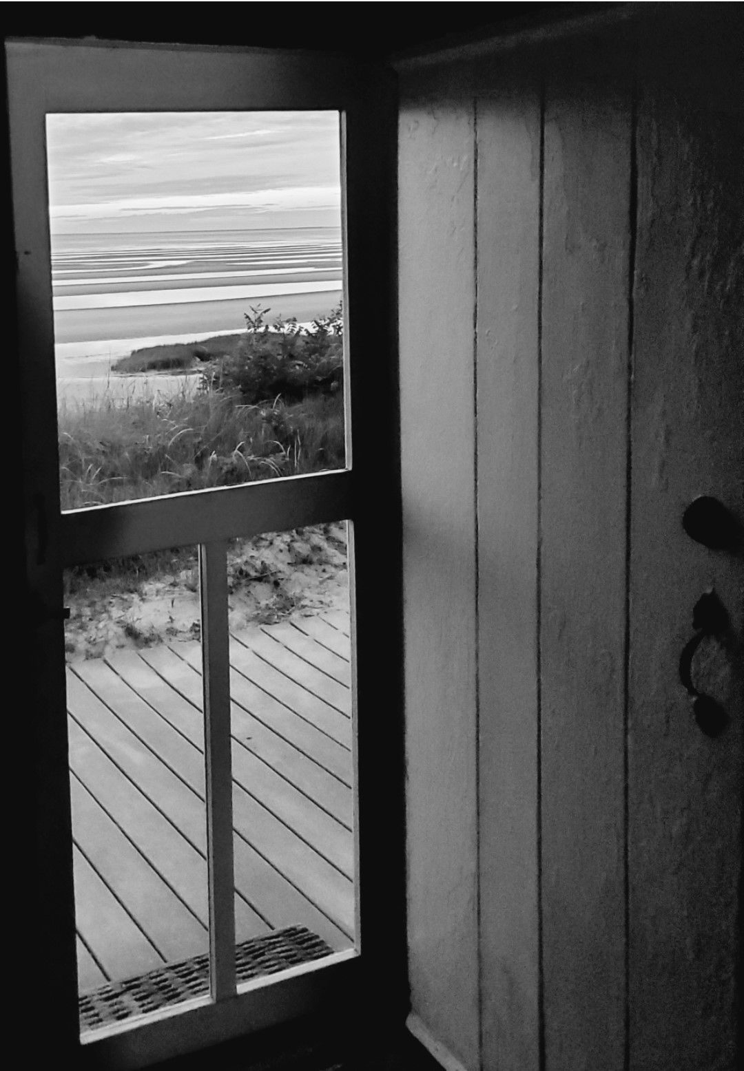 A black and white photo of a window with a view of the ocean