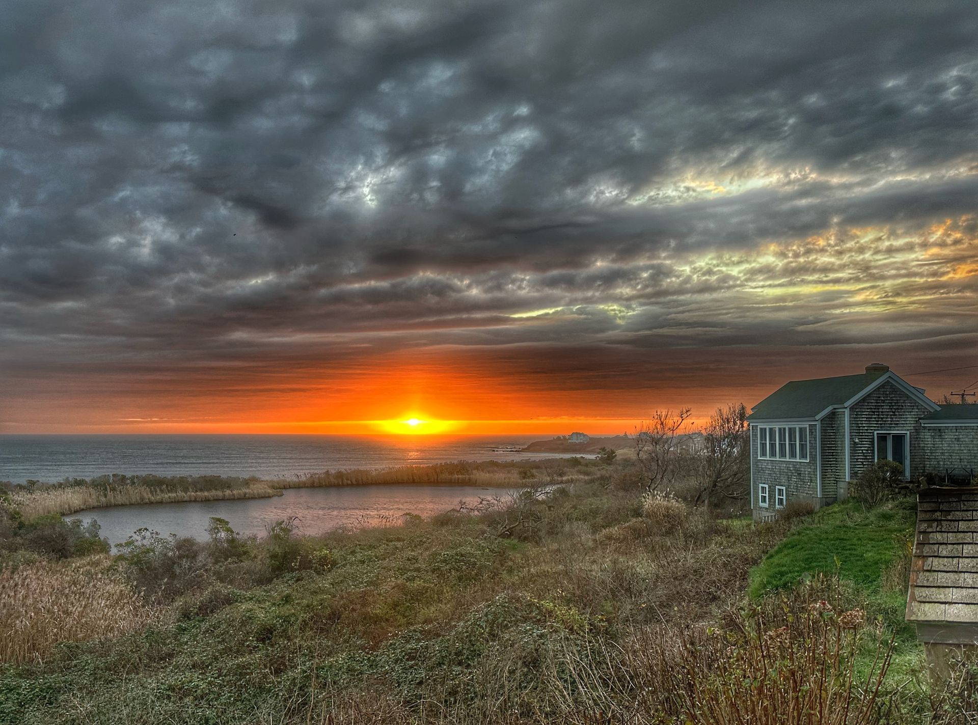 a sunset over the ocean with a house in the foreground