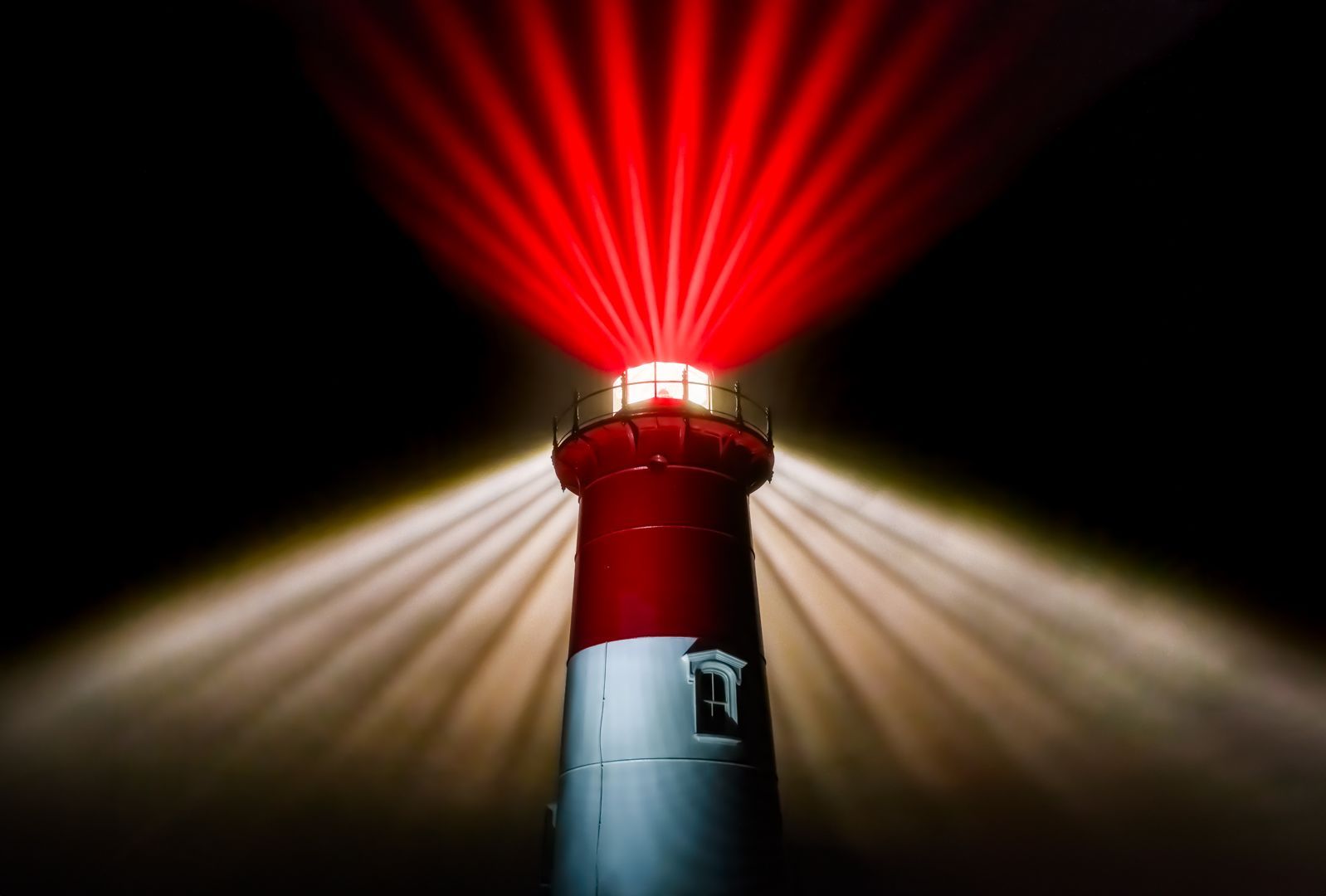 A red and white lighthouse is lit up at night