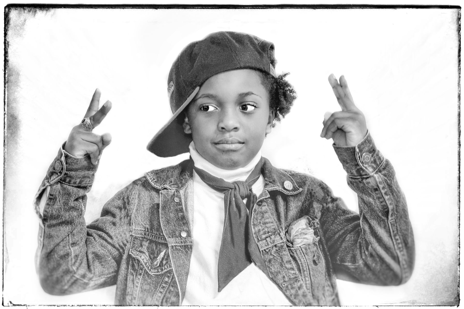 A young boy wearing a hat and tie is giving a peace sign