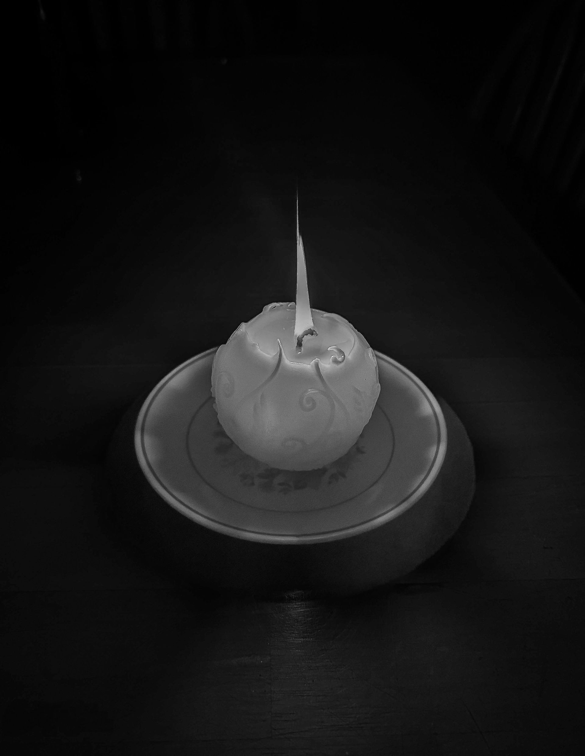 A black and white photo of a lit candle on a saucer