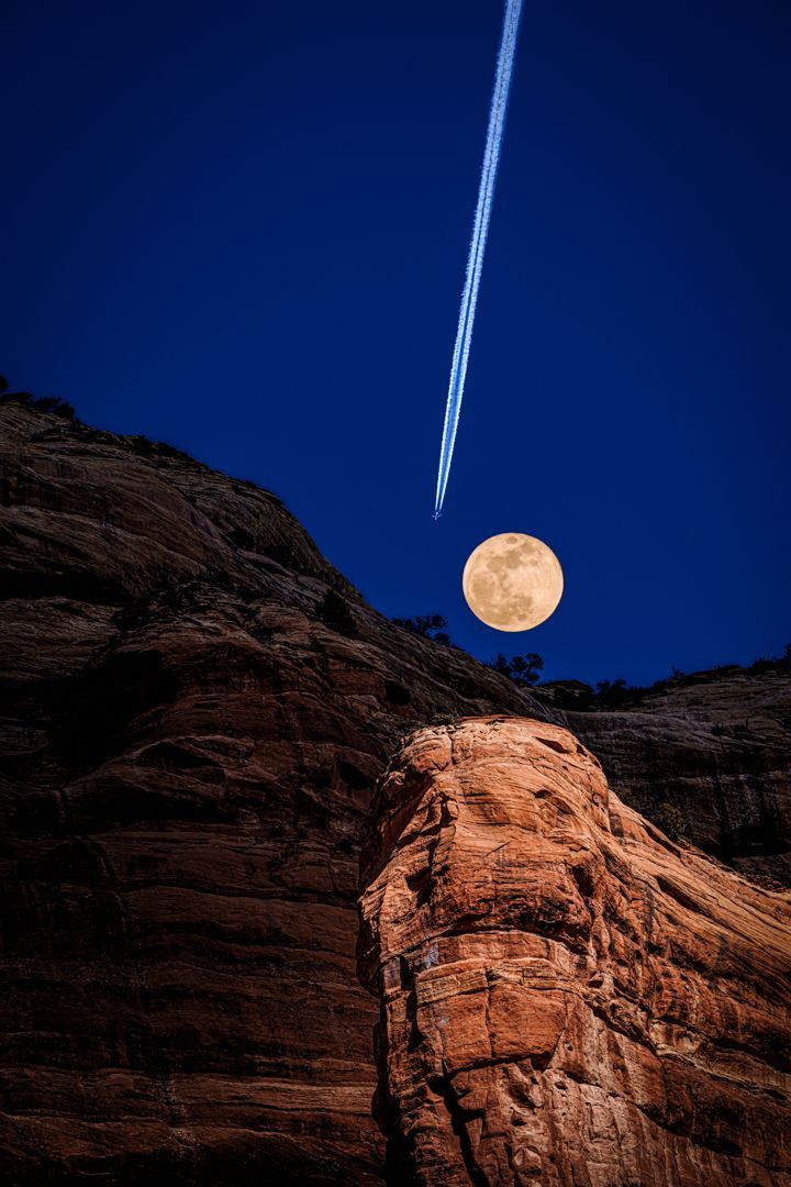 A full moon is rising over a rocky cliff at night.