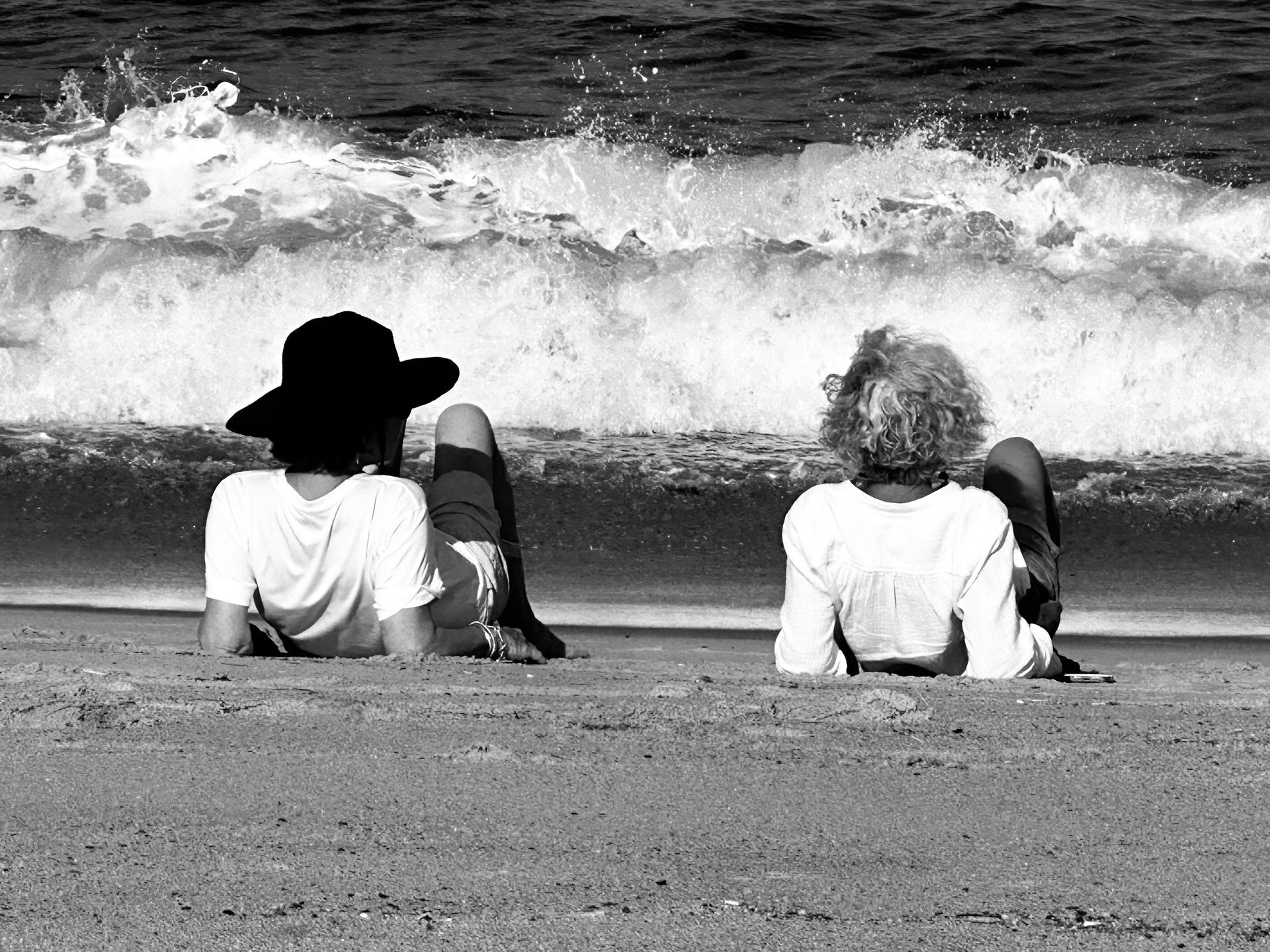 Two people are sitting on the beach looking at the ocean waves.