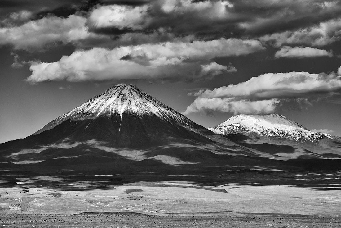 a black and white photo of two mountains covered in snow under a cloudy sky .