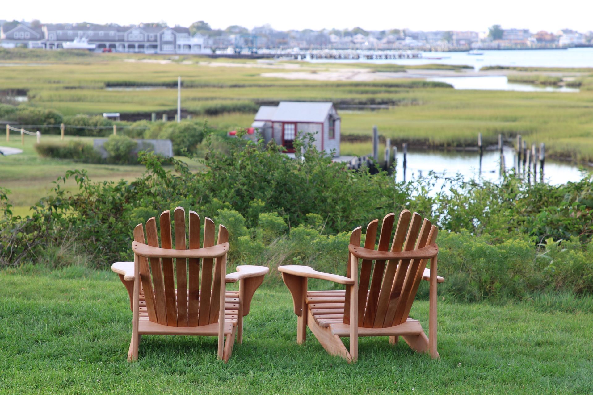two wooden adirondack chairs are sitting in the grass with a view of a marsh .