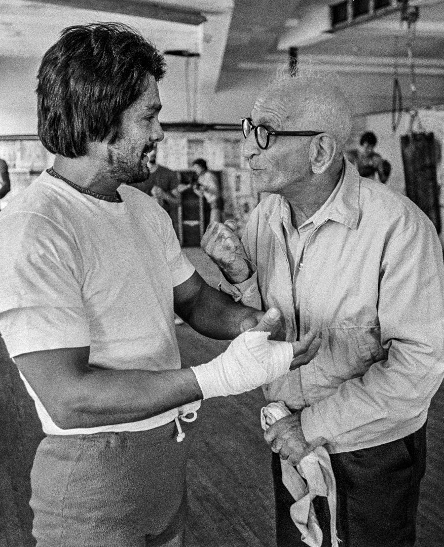 A black and white photo of two men talking in a gym.