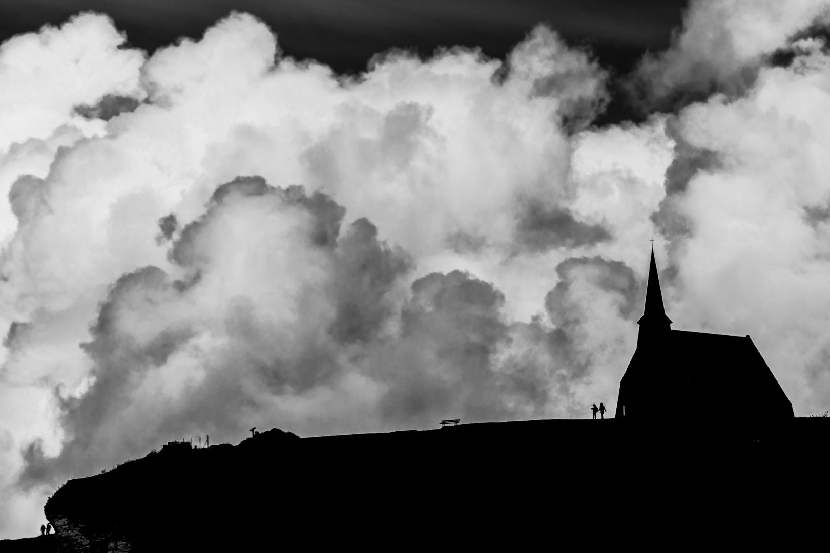 A black and white photo of a church silhouetted against a cloudy sky.