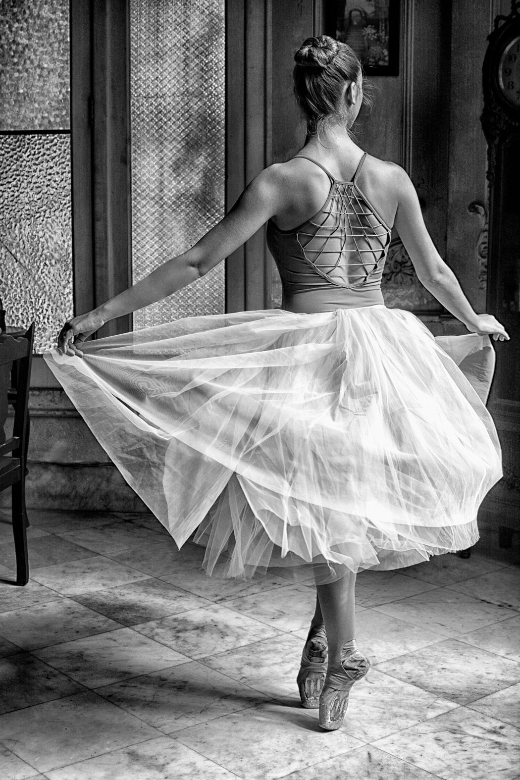 A black and white photo of a ballerina dancing in a room.