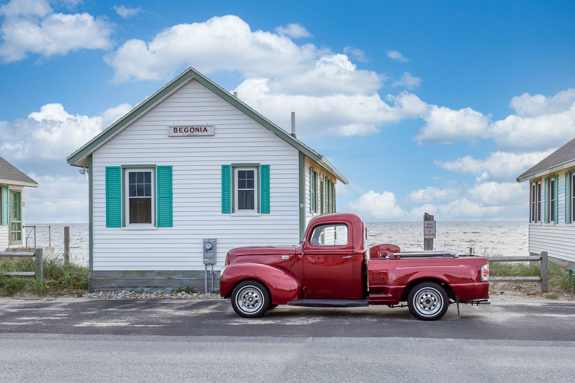 a red truck is parked in front of a small white house with green shutters .