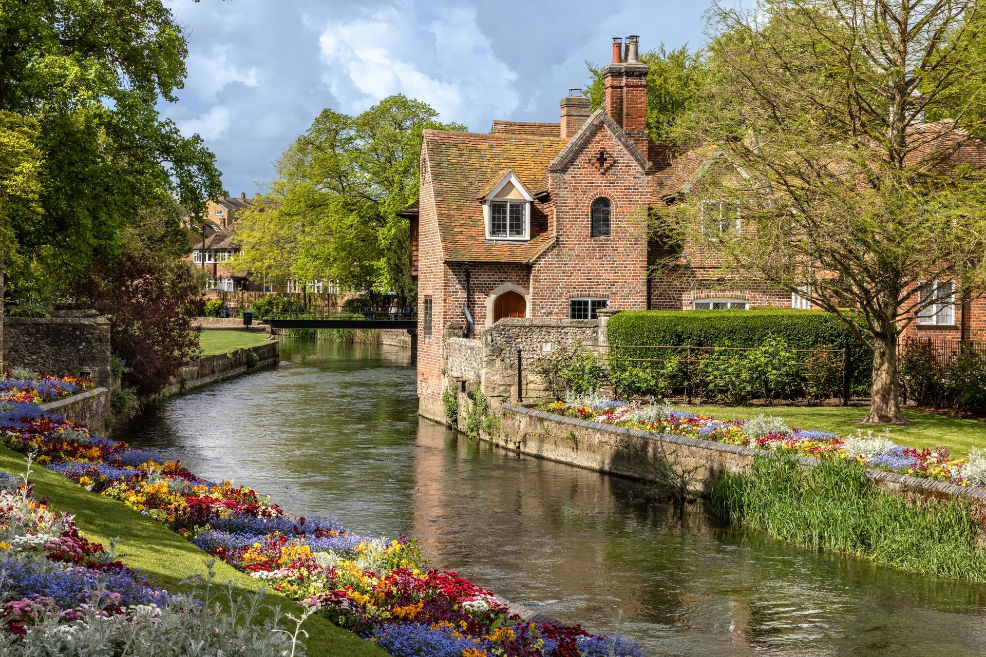 a brick house sitting next to a river with flowers in front of it .