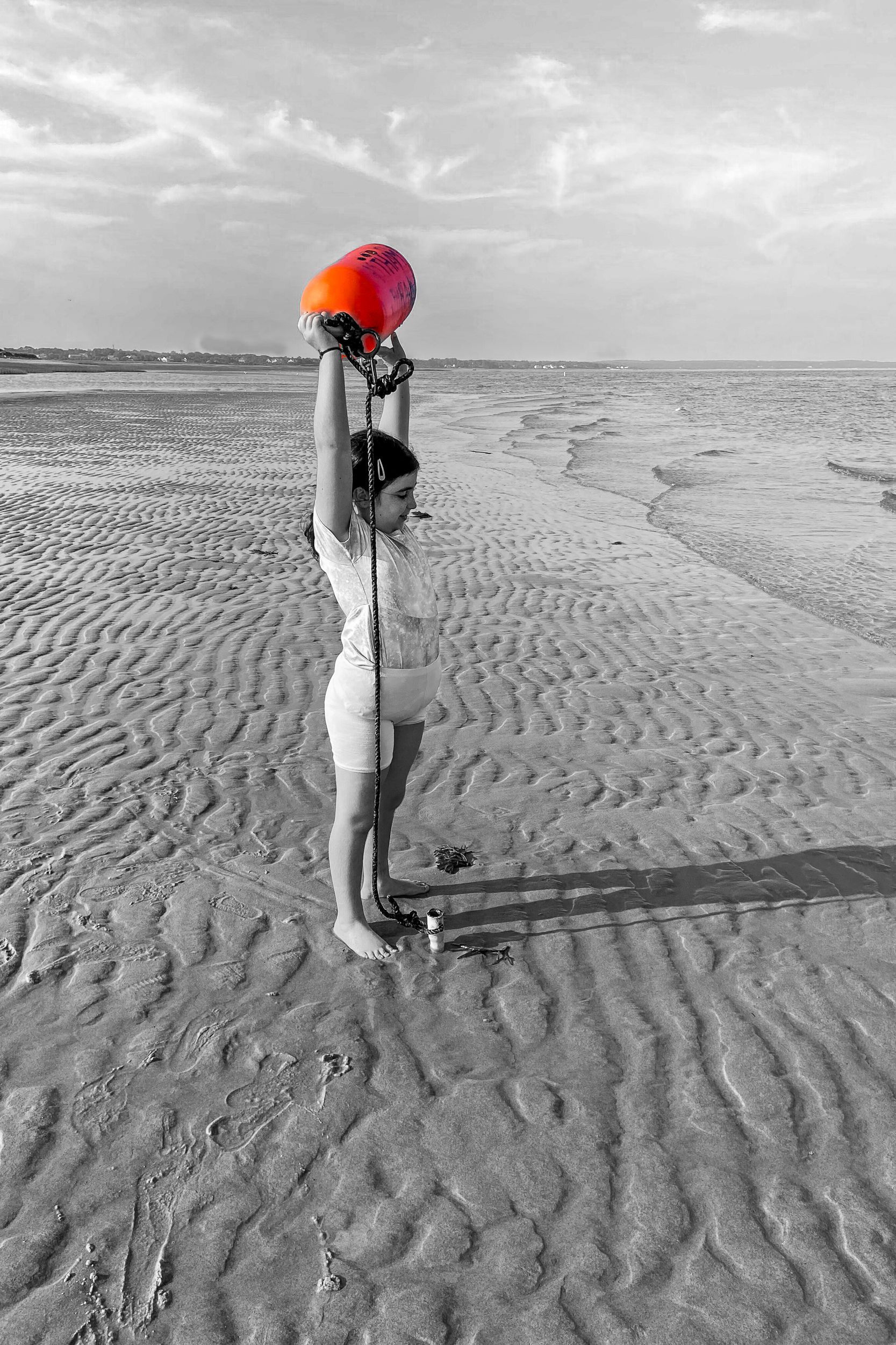 A woman is holding an orange balloon on the beach.