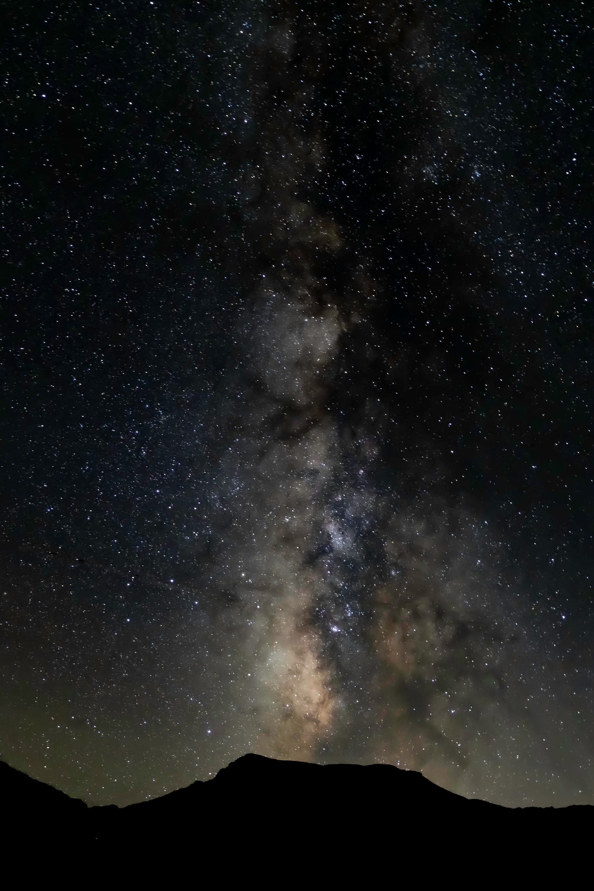 a night sky filled with lots of stars and a mountain in the foreground .