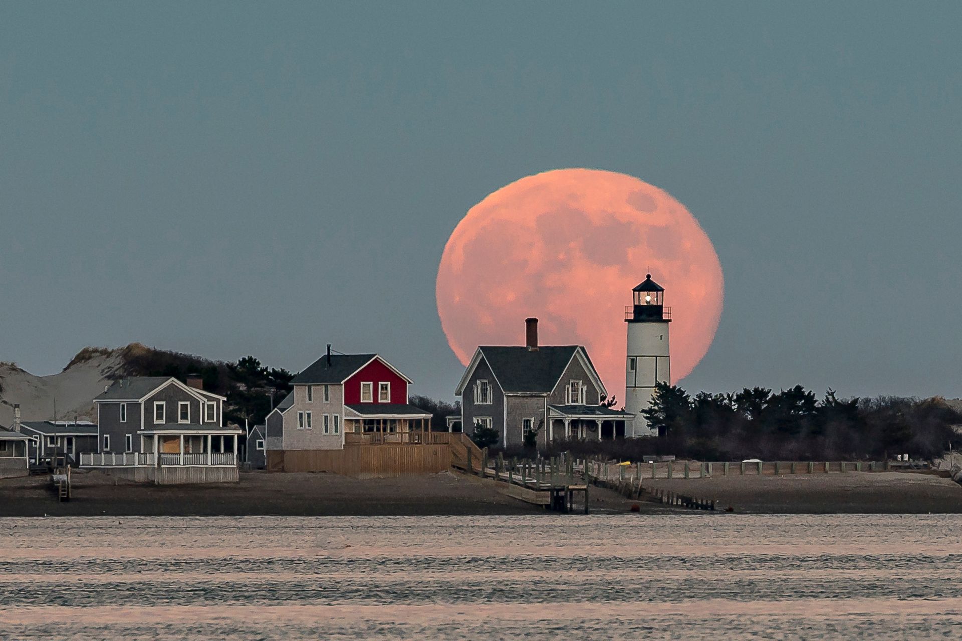 a full moon is rising over a lighthouse and houses